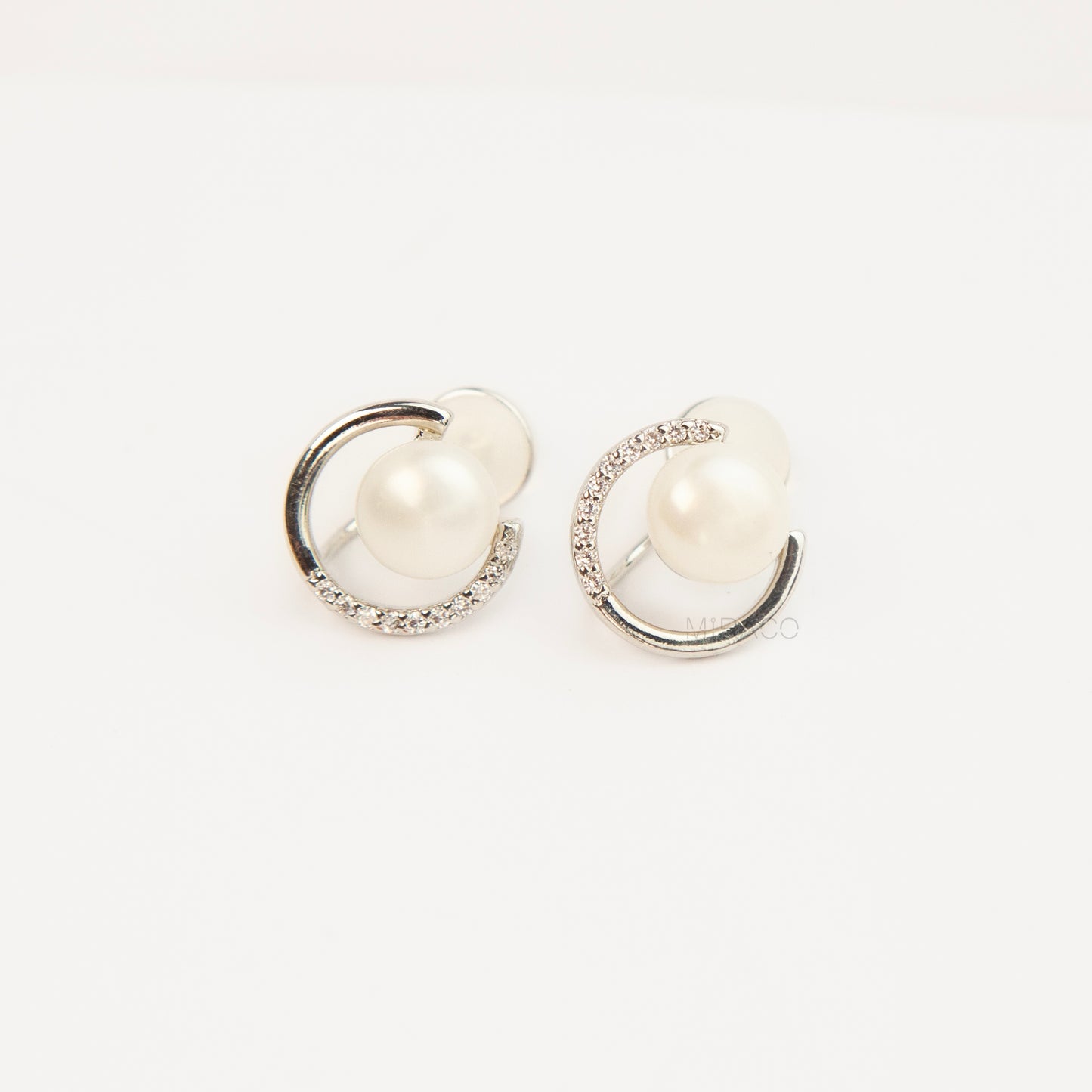 Pair of non-pierced silver-tone clip-on earrings with round silicone backs, featuring a real white freshwater pearl wrapped in a sparkling cubic zirconia crescent loop.