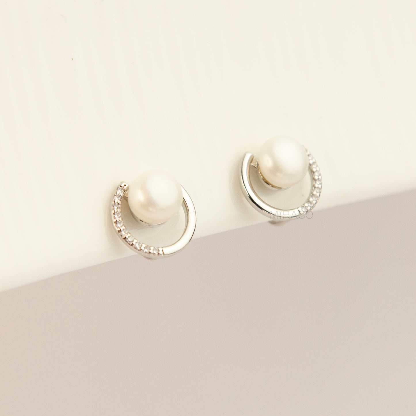 Pair of non-pierced silver-tone clip-on earrings with round silicone backs, featuring a real white freshwater pearl wrapped in a sparkling cubic zirconia crescent loop.