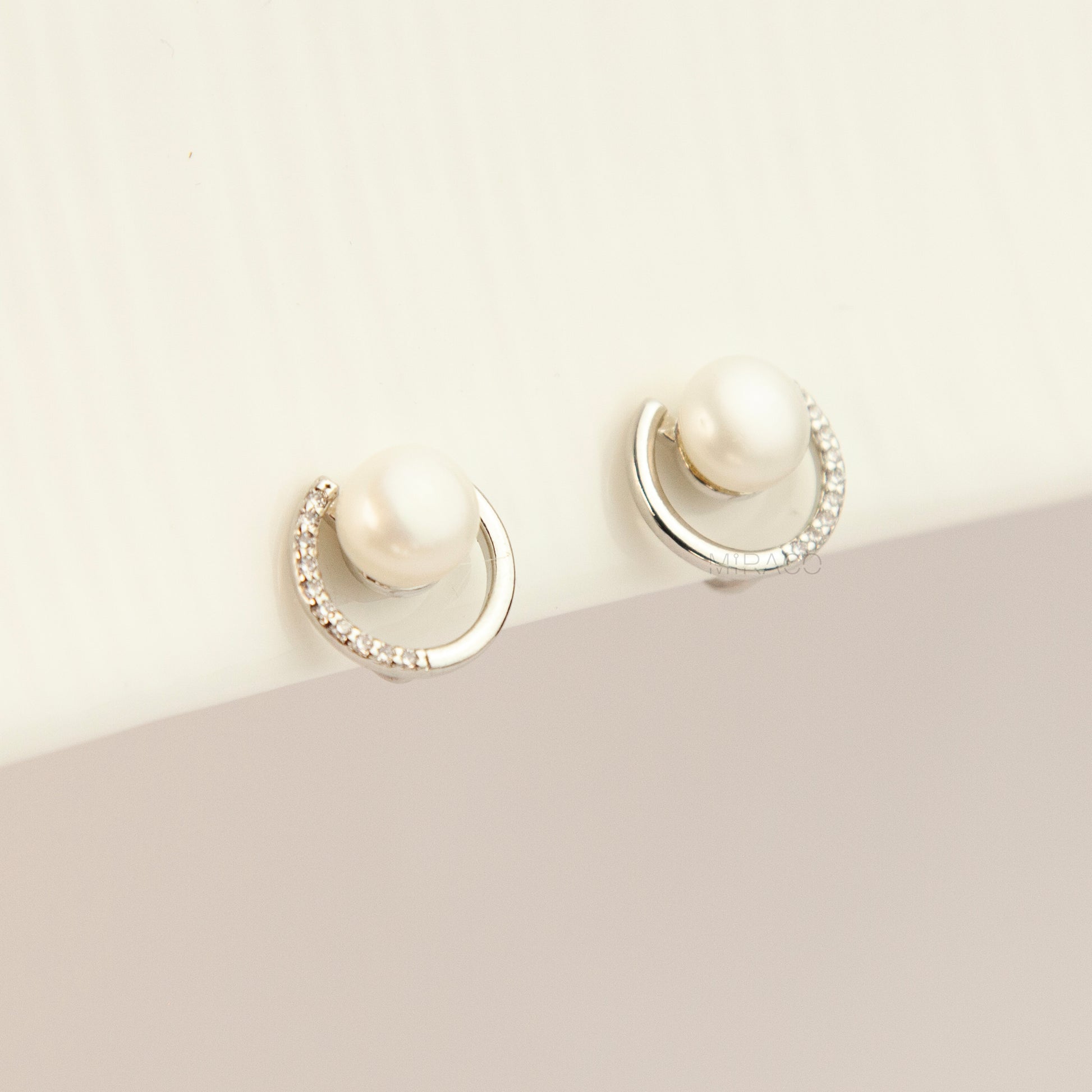 Pair of non-pierced silver-tone clip-on earrings with round silicone backs, featuring a real white freshwater pearl wrapped in a sparkling cubic zirconia crescent loop.