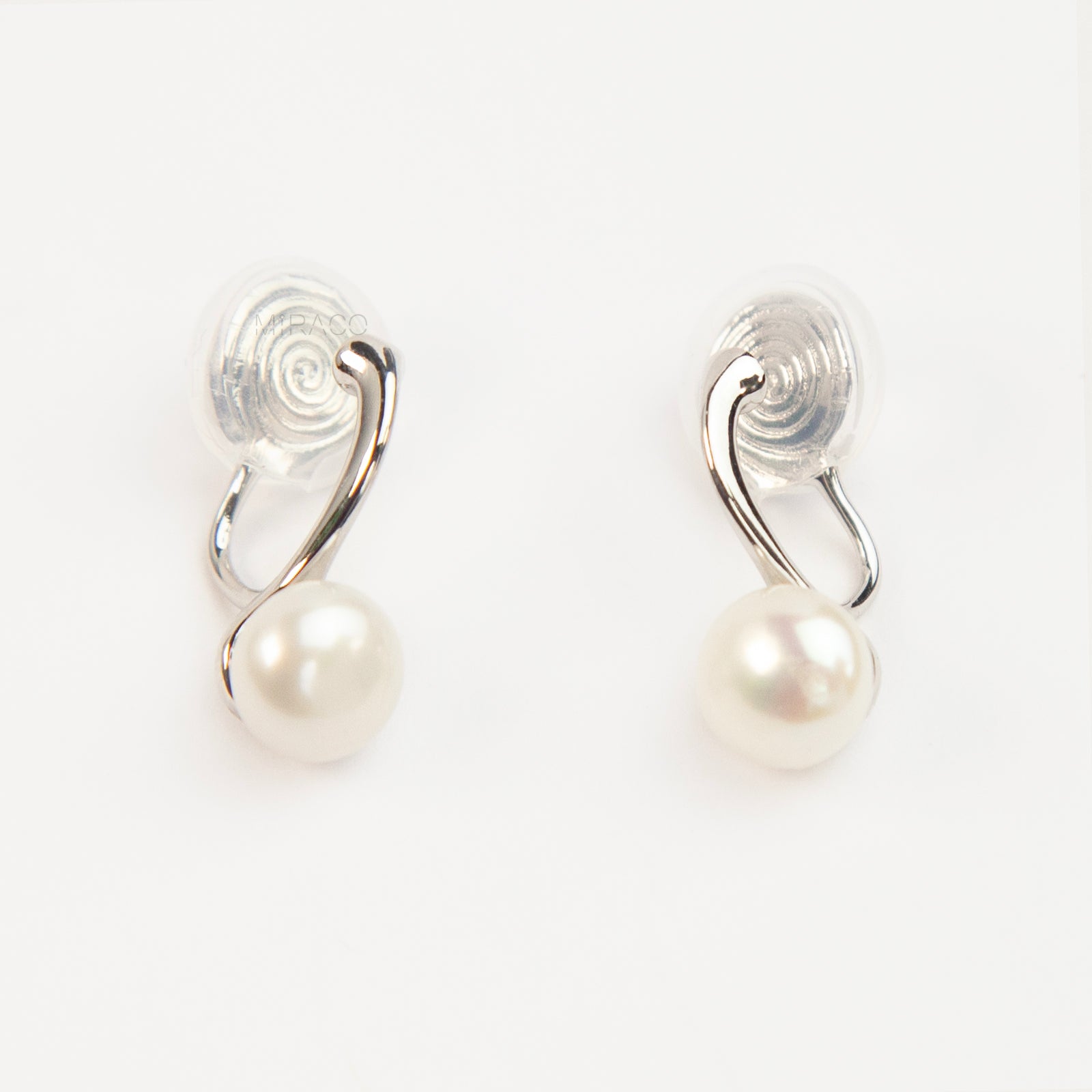 A pair of silver-tone clip-on earrings featuring a single round genuine white pearl dangling from a sleek curved metal bar, equipped with adjustable coil-spring backs