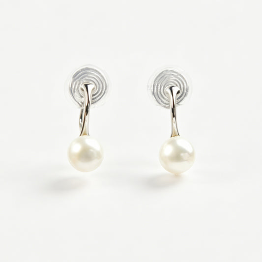 A pair of silver-tone clip-on earrings featuring a single round genuine white pearl dangling from a sleek curved metal bar, equipped with adjustable coil-spring backs