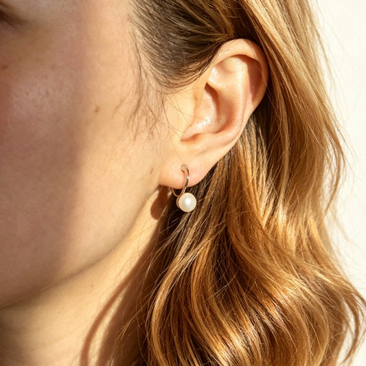A pair of silver-tone clip-on earrings featuring a single round genuine white pearl dangling from a sleek curved metal bar, equipped with adjustable coil-spring backs