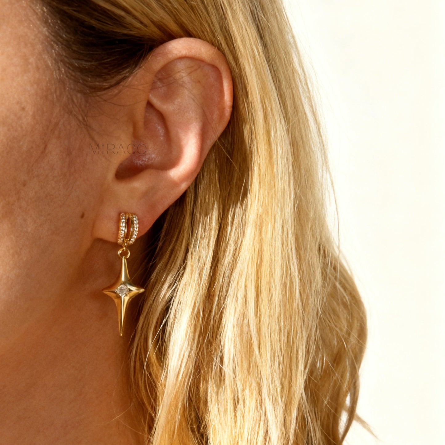 A pair of gold-toned dangle clip-on earrings featuring a modern, four-point North Star pendant centered with a clear rhinestone. The top closure is a comfortable coil-back style, partially covered with pave-set rhinestones.