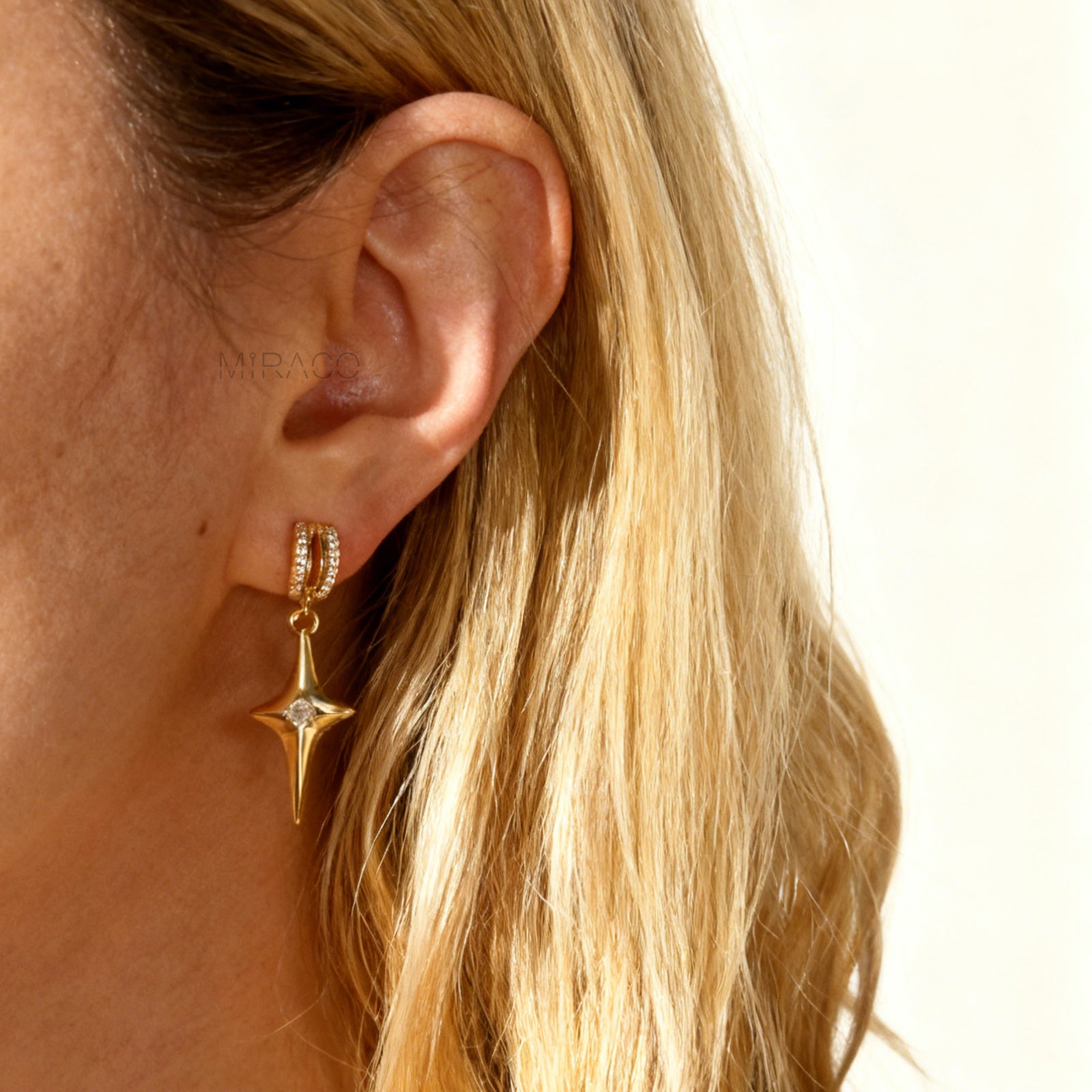 A pair of gold-toned dangle clip-on earrings featuring a modern, four-point North Star pendant centered with a clear rhinestone. The top closure is a comfortable coil-back style, partially covered with pave-set rhinestones.