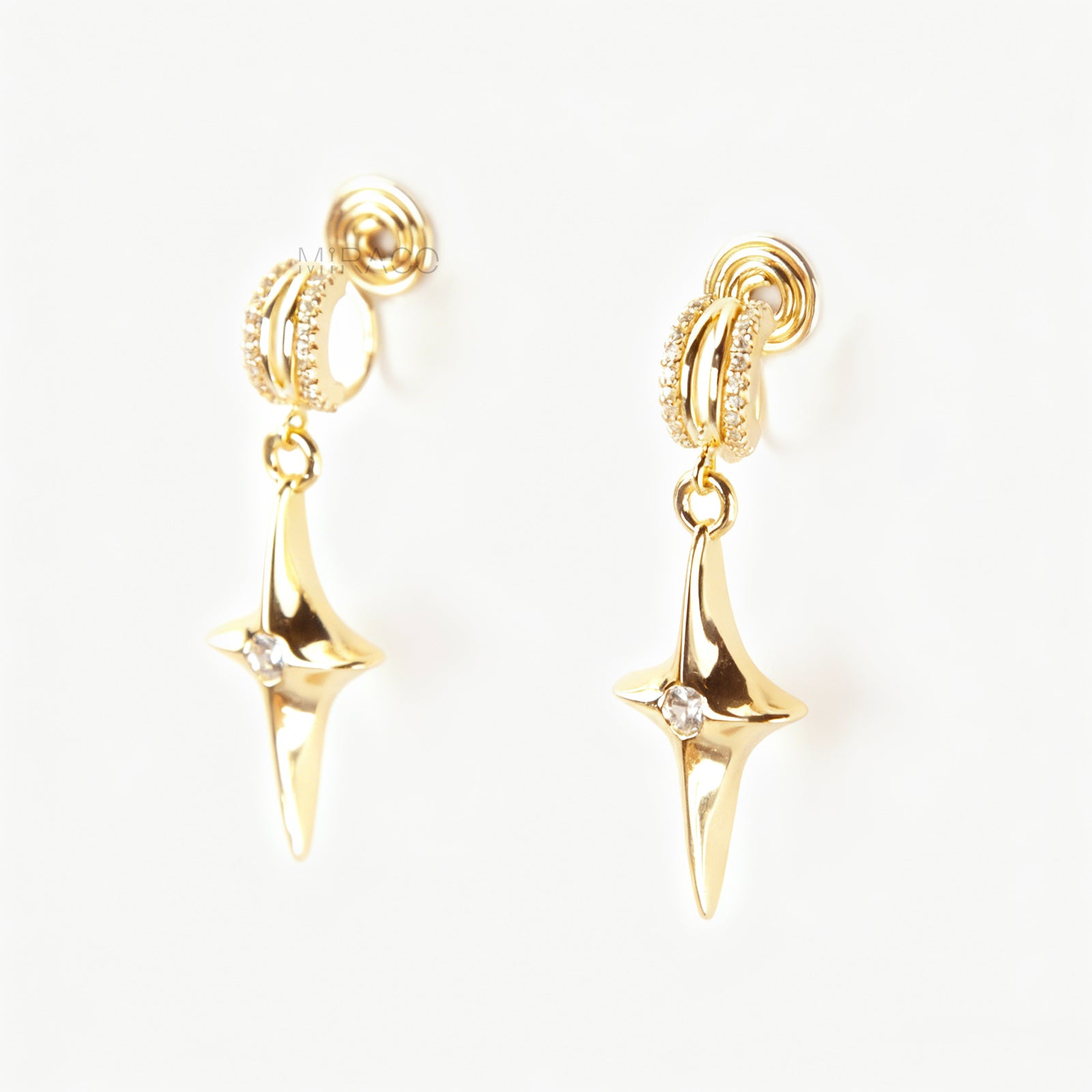 A pair of gold-toned dangle clip-on earrings featuring a modern, four-point North Star pendant centered with a clear rhinestone. The top closure is a comfortable coil-back style, partially covered with pave-set rhinestones.