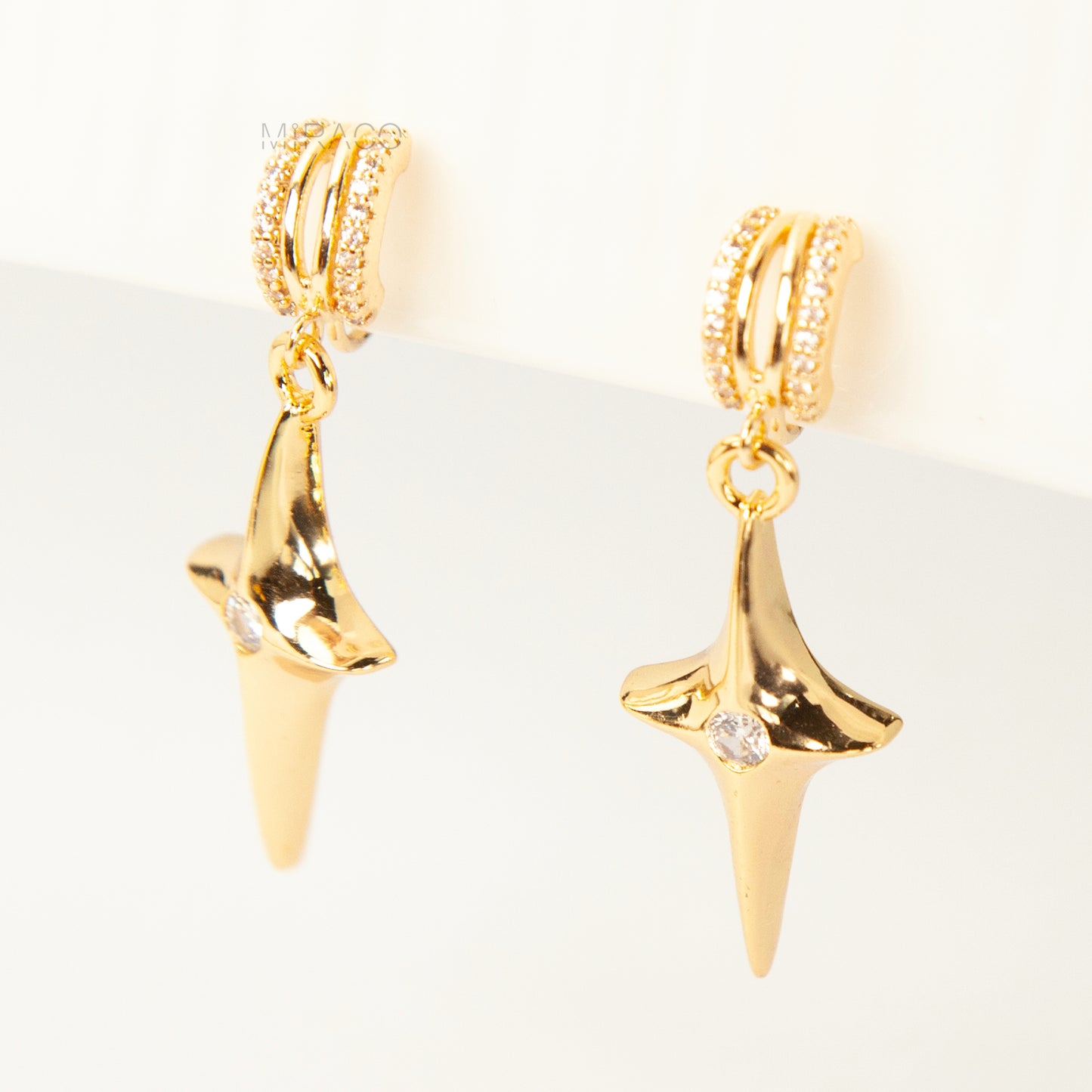 A pair of gold-toned dangle clip-on earrings featuring a modern, four-point North Star pendant centered with a clear rhinestone. The top closure is a comfortable coil-back style, partially covered with pave-set rhinestones.