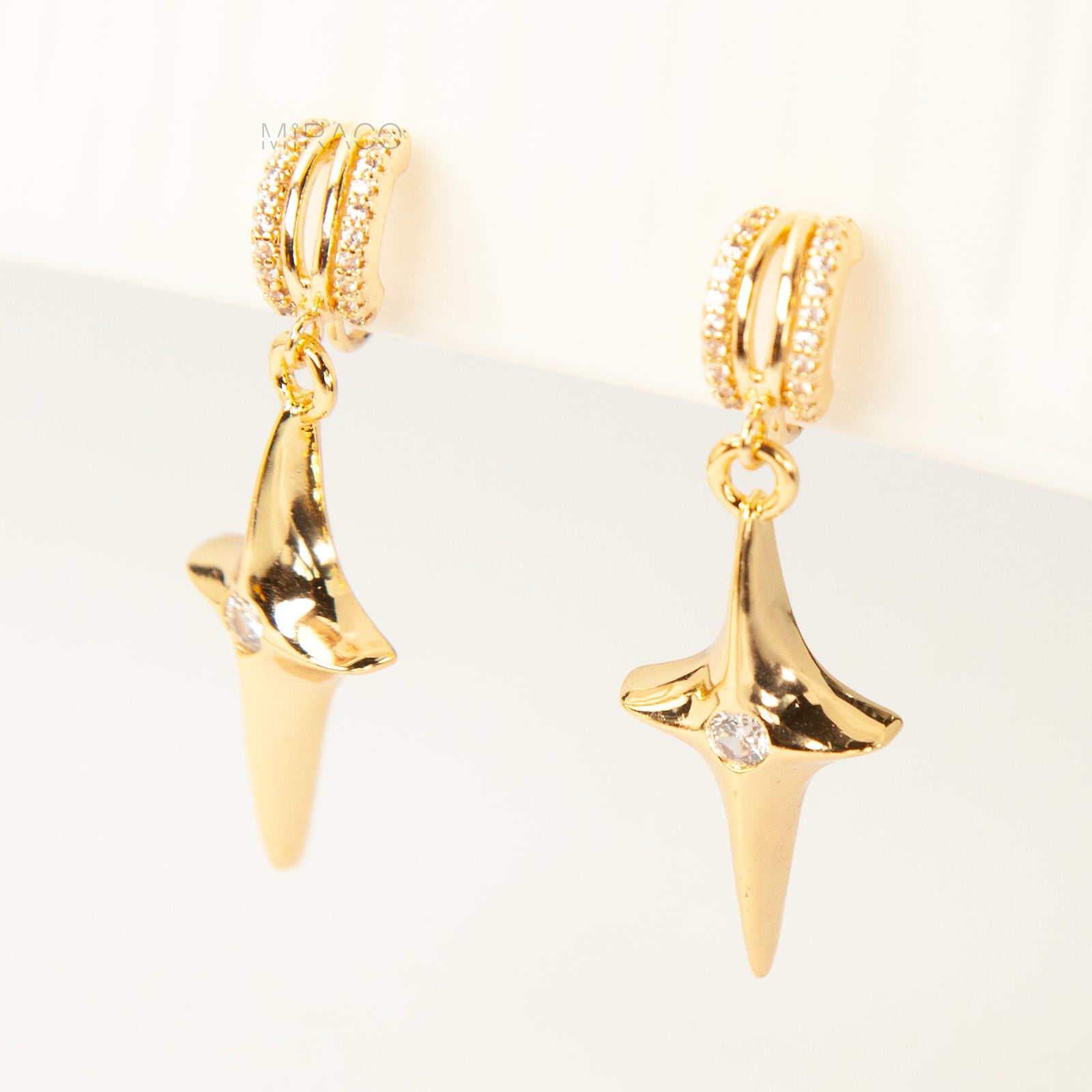 A pair of gold-toned dangle clip-on earrings featuring a modern, four-point North Star pendant centered with a clear rhinestone. The top closure is a comfortable coil-back style, partially covered with pave-set rhinestones.