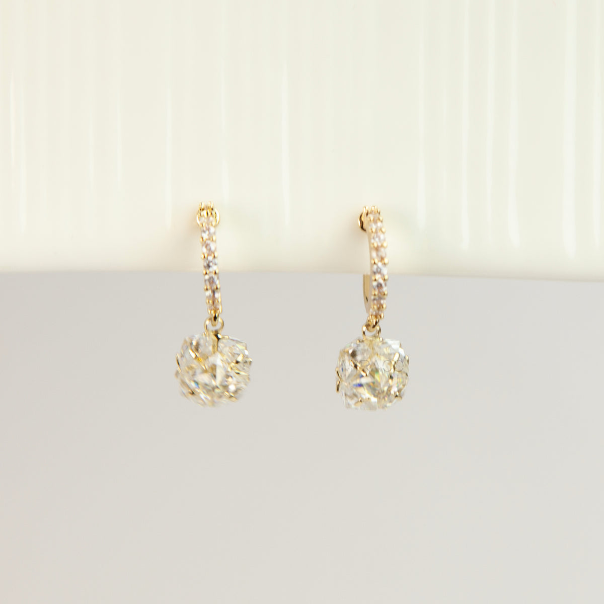 Pair of gold-toned non-pierced clip-on hoop earrings with pavé crystals, clear faceted glass sphere drops, and spiral coil backs with silicone pads.