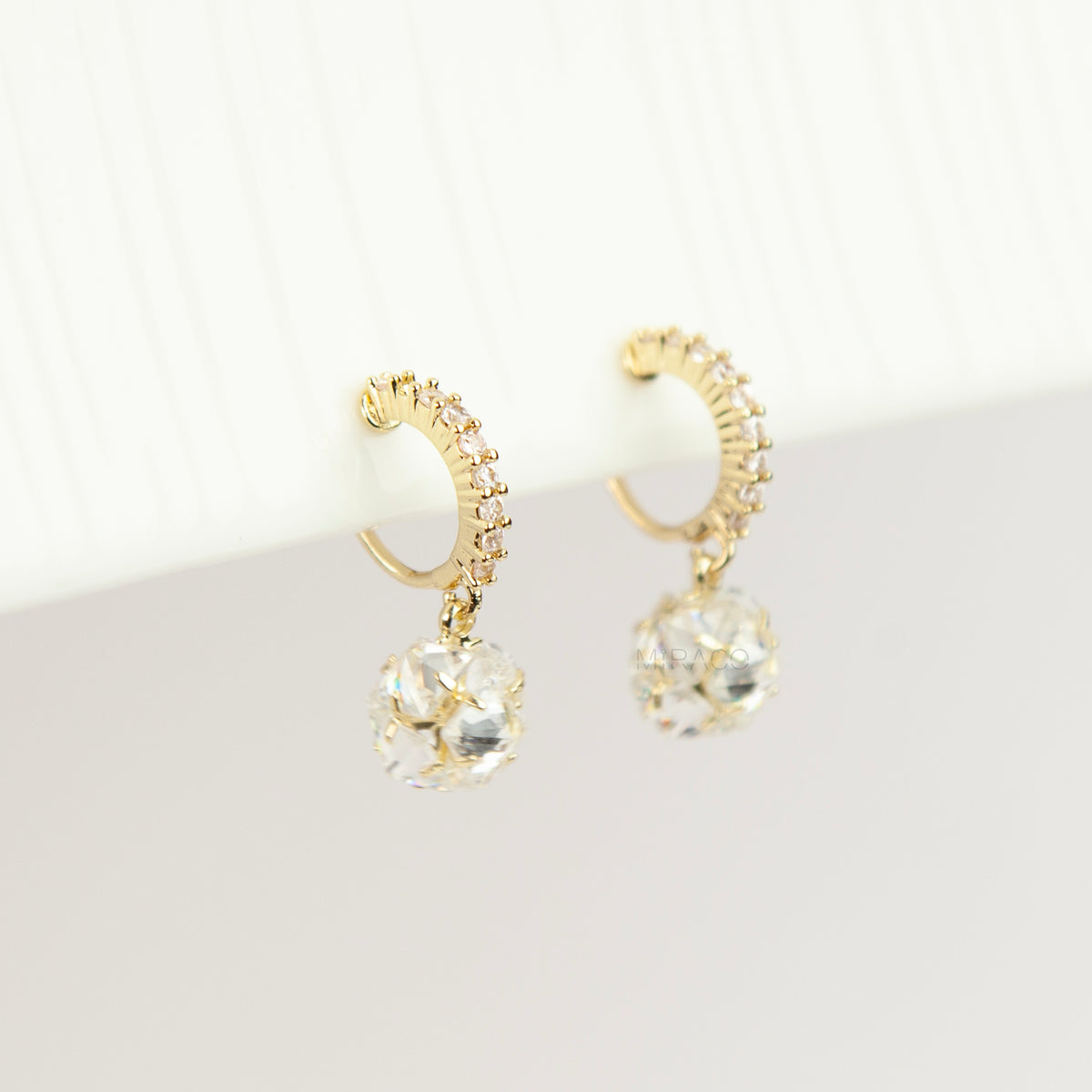 Pair of gold-toned non-pierced clip-on hoop earrings with pavé crystals, clear faceted glass sphere drops, and spiral coil backs with silicone pads.