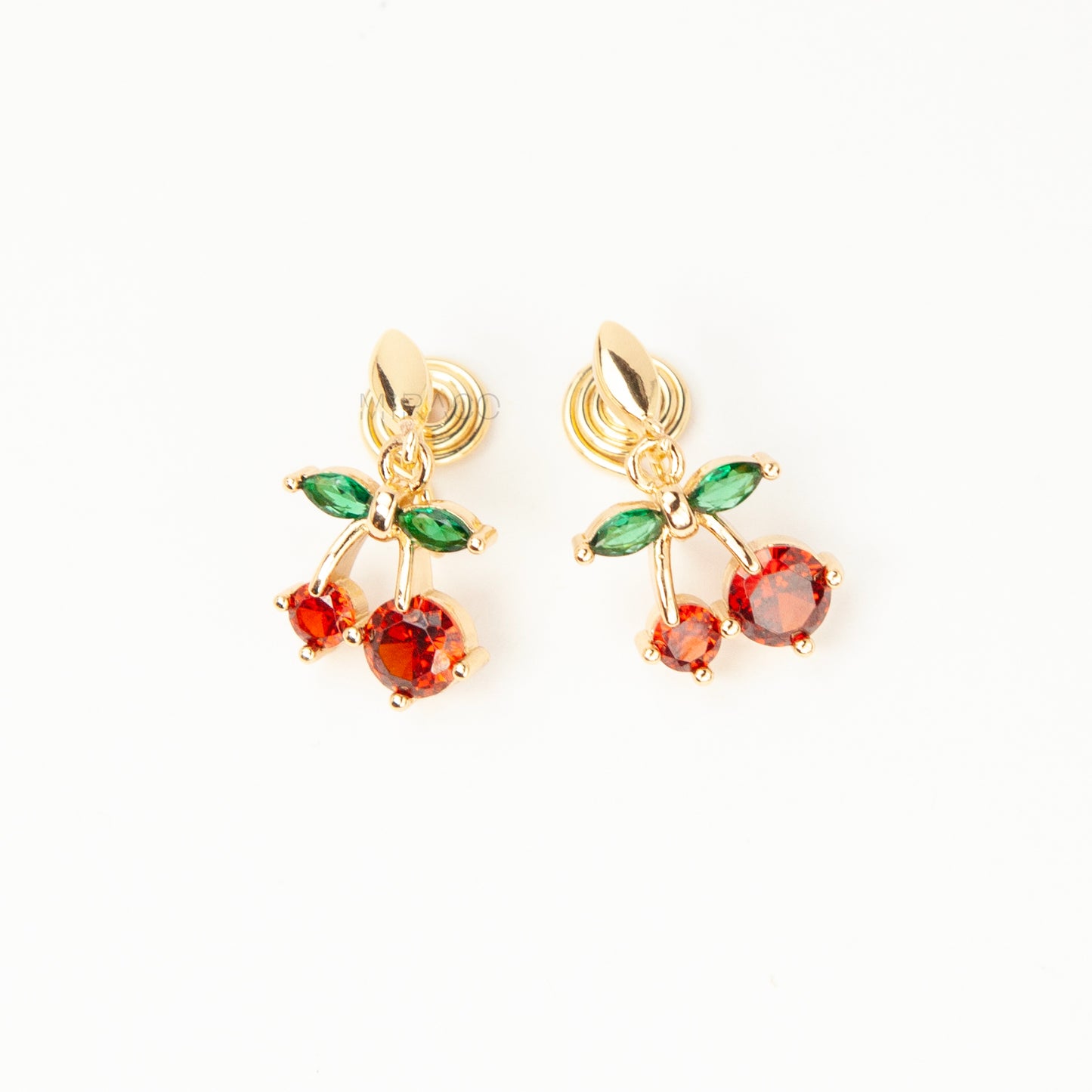 Pair of gold-plated coil back clip-on earrings featuring a double-cherry dangle design. The cherries are made of faceted red cubic zirconia stones with green marquise-cut CZ leaves above them. The back is a round, spiraled coil for comfort.