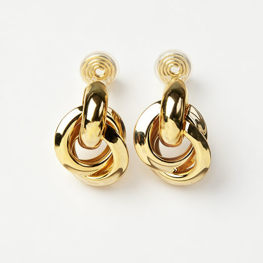 A pair of high-polish gold clip-on earrings featuring three interlocking, dimensional smooth metal hoops arranged in a interlocking knot pattern, attached to clear-padded adjustable metal coil backs.