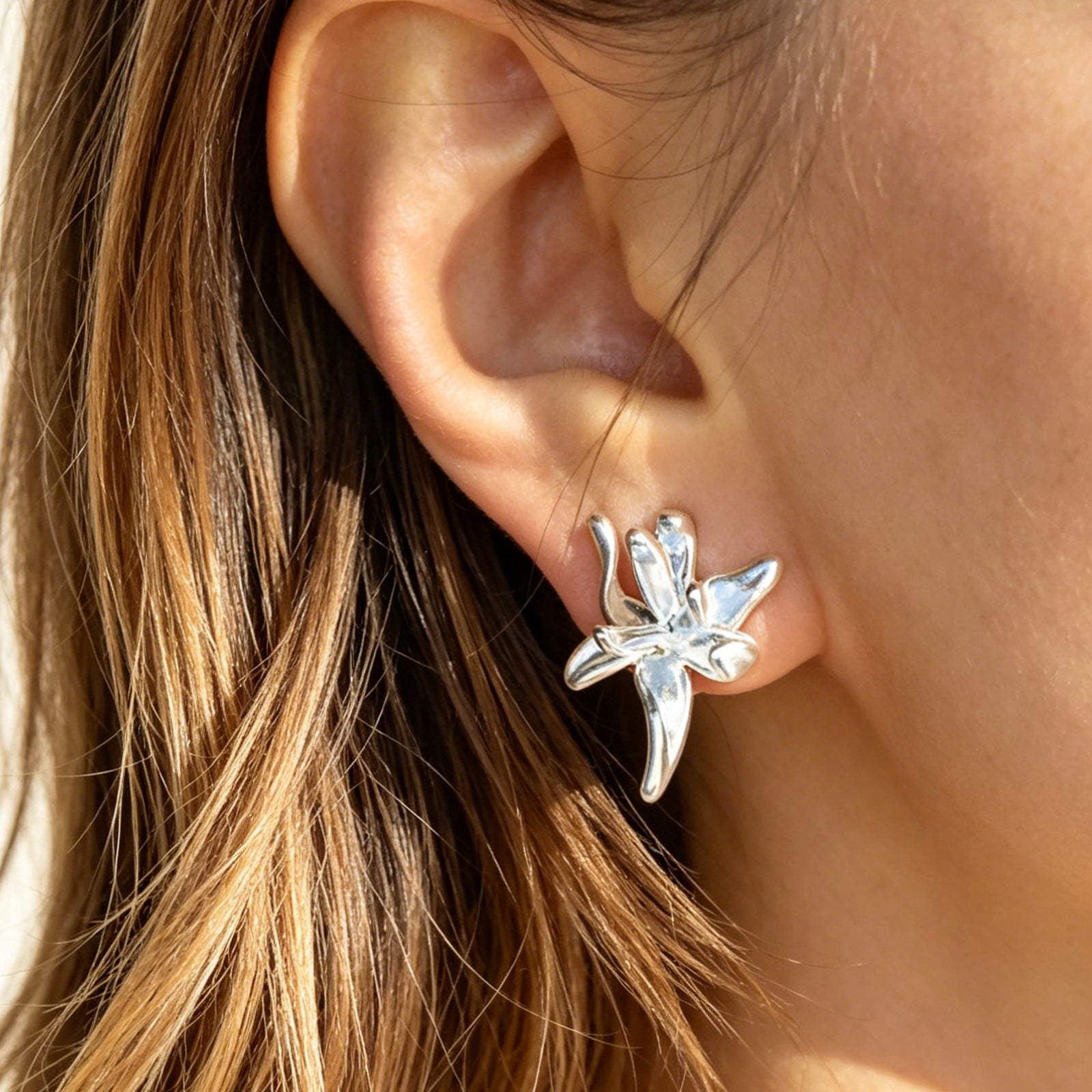 elegant matte silver floral clip-on earrings, showcasing an abstract 3D orchid flower design with organic, curved metallic petals and fitted with comfortable, invisible-style adjustable coil backs for non-pierced ears.