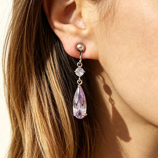 Close-up of a person wearing a teardrop-shaped purple earring.