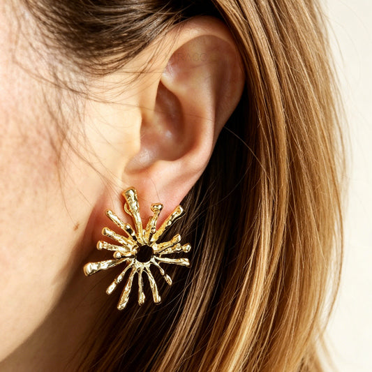 Gold sunburst earring worn by a person with blonde hair.