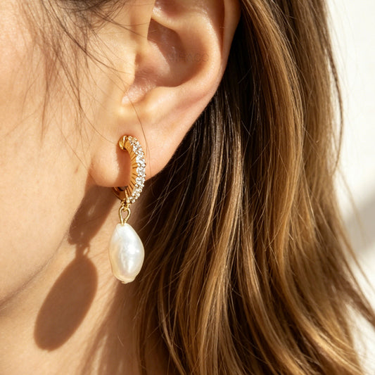 Close-up of an ear wearing a gold hoop earring with a pearl drop earring.