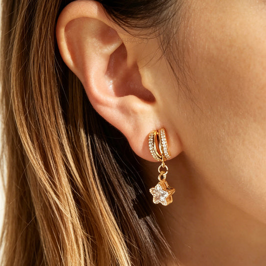 Close-up of an ear wearing a gold hoop earring with a star charm.