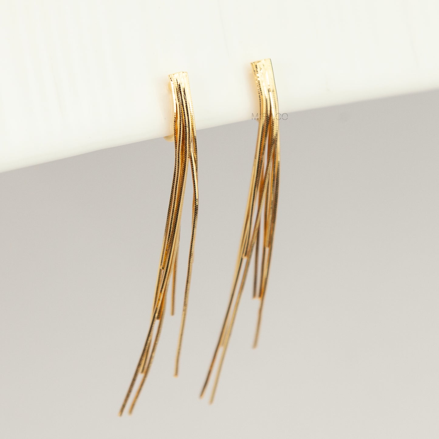 Gold statement clip-on earrings with coil backs featuring long cascading liquid snake tassel chains on a clean white background