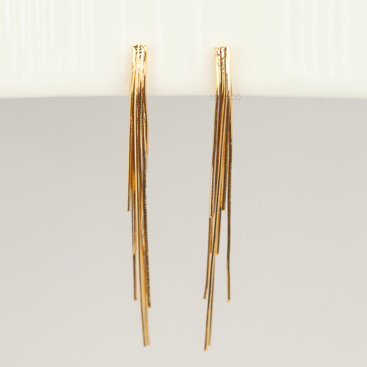 Gold statement clip-on earrings with coil backs featuring long cascading liquid snake tassel chains on a clean white background