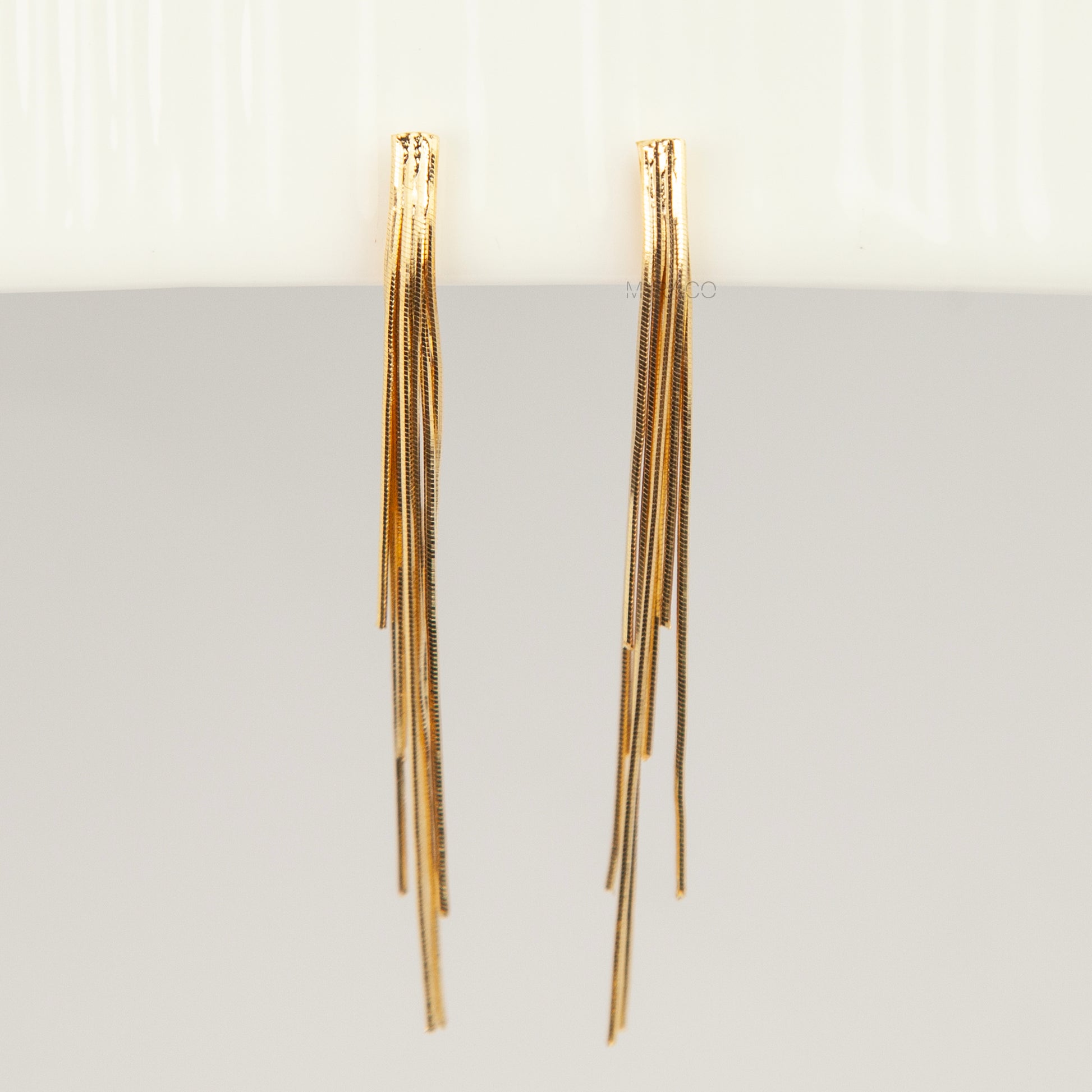 Gold statement clip-on earrings with coil backs featuring long cascading liquid snake tassel chains on a clean white background