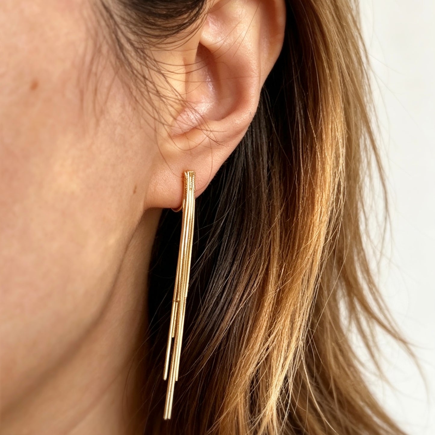 Gold statement clip-on earrings with coil backs featuring long cascading liquid snake tassel chains on a clean white background