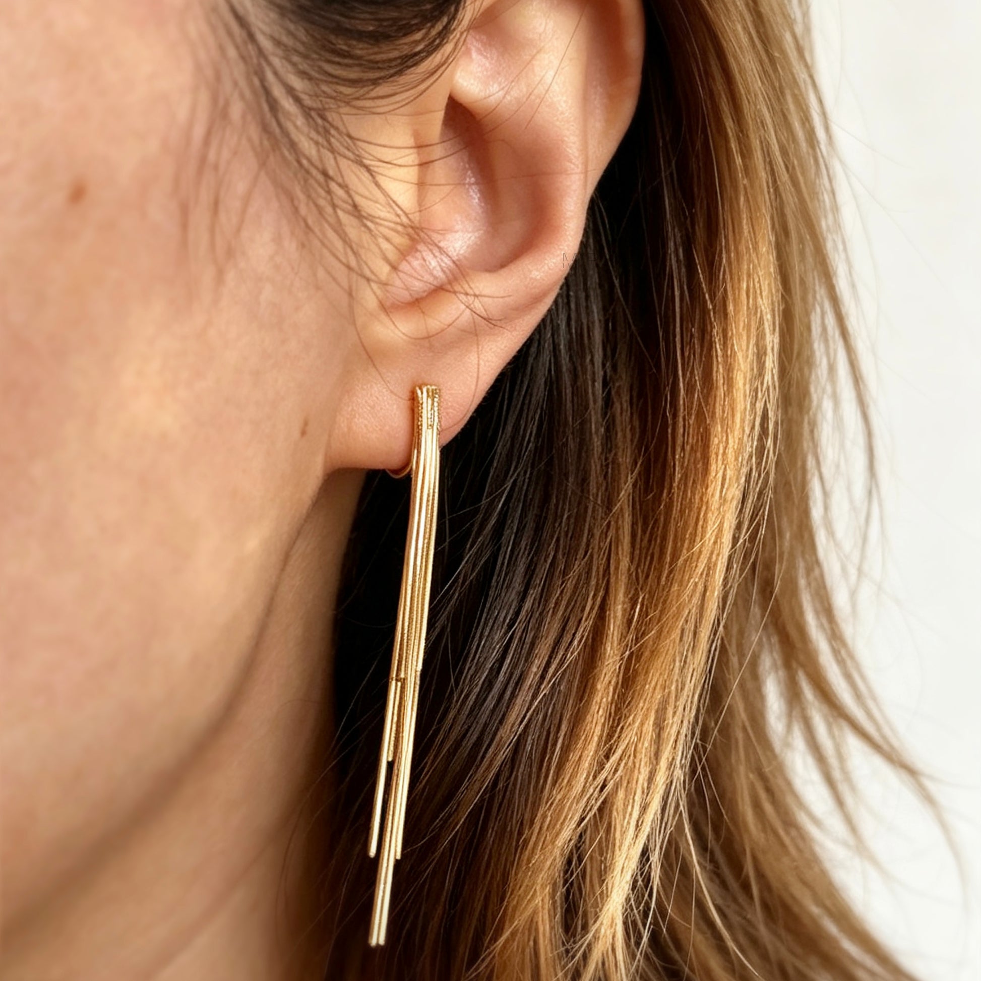 Gold statement clip-on earrings with coil backs featuring long cascading liquid snake tassel chains on a clean white background