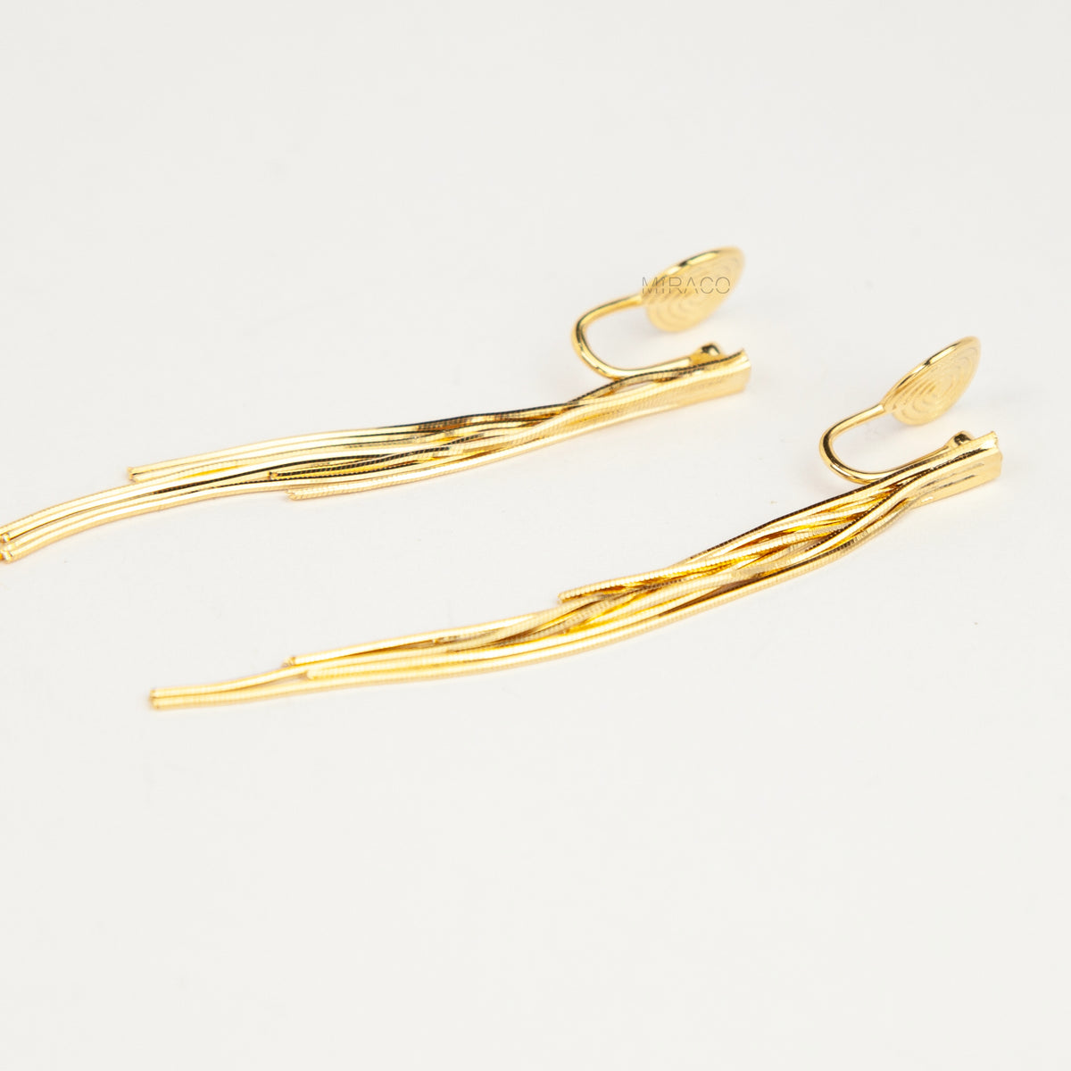Gold statement clip-on earrings with coil backs featuring long cascading liquid snake tassel chains on a clean white background