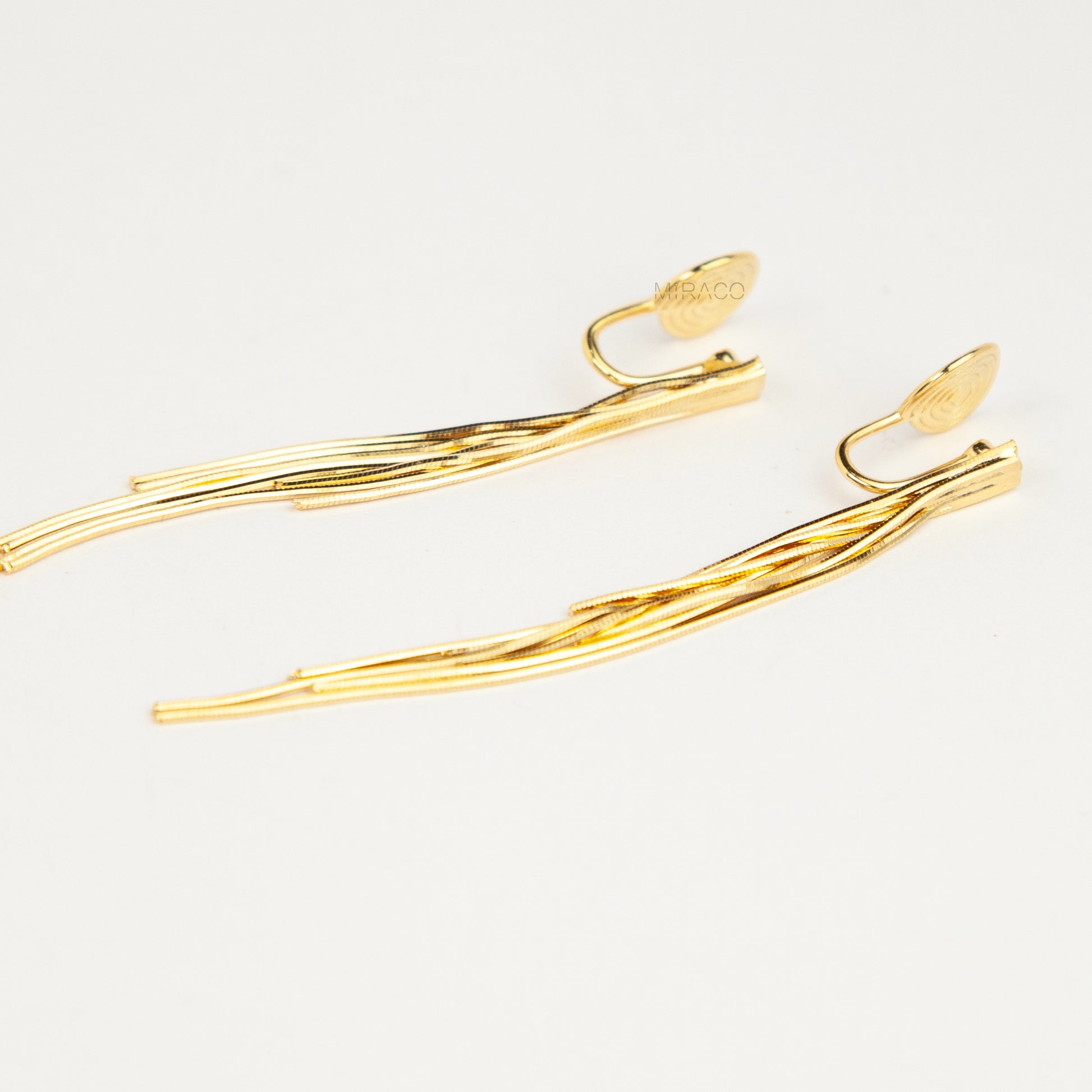 Gold statement clip-on earrings with coil backs featuring long cascading liquid snake tassel chains on a clean white background