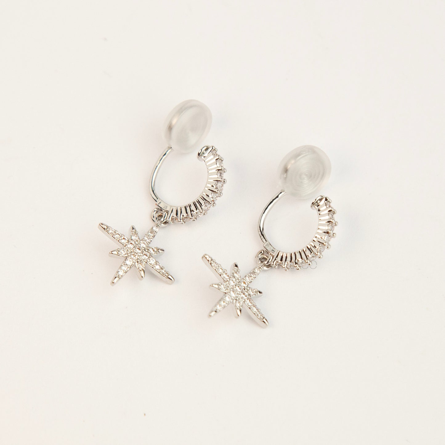 Gold and silver non-pierced clip-on dangle earrings with coil backs, featuring cubic zirconia paved hoops and celestial starburst drops.