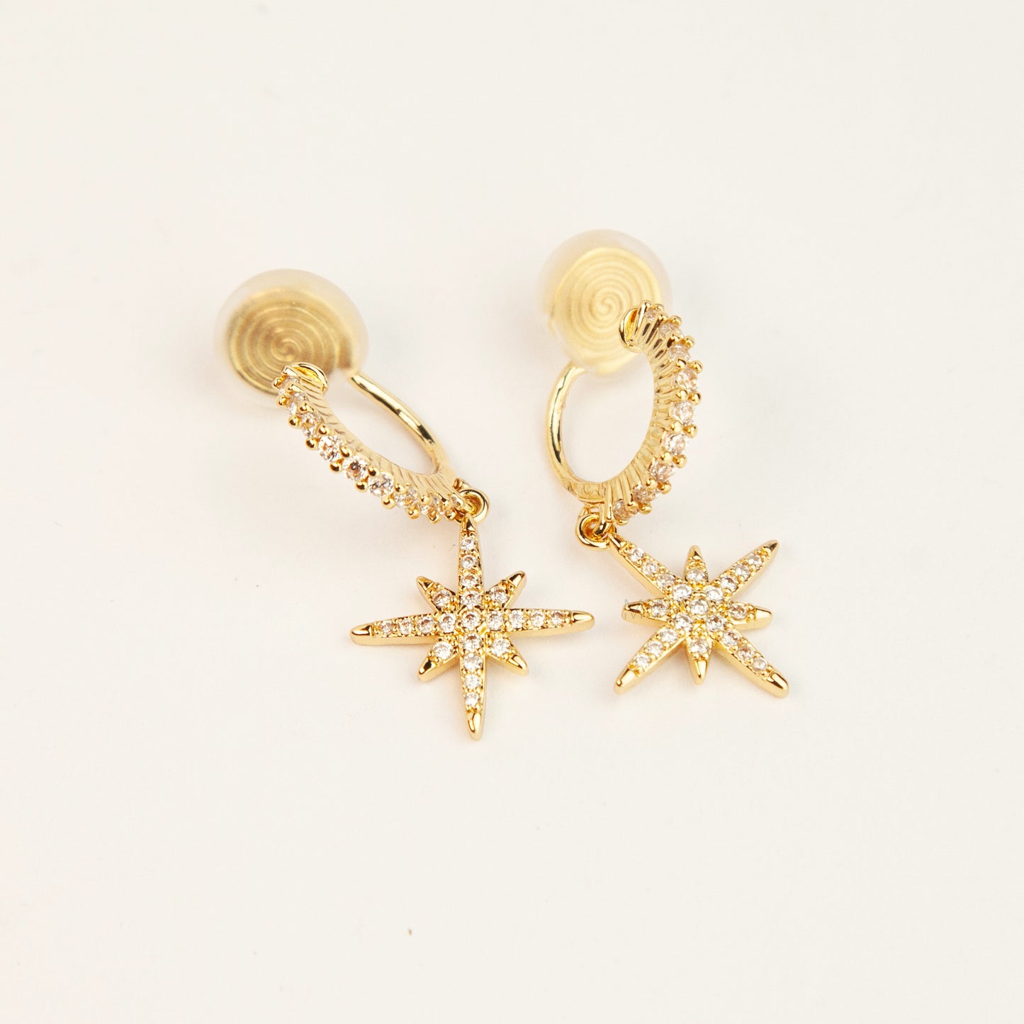 Gold and silver non-pierced clip-on dangle earrings with coil backs, featuring cubic zirconia paved hoops and celestial starburst drops.