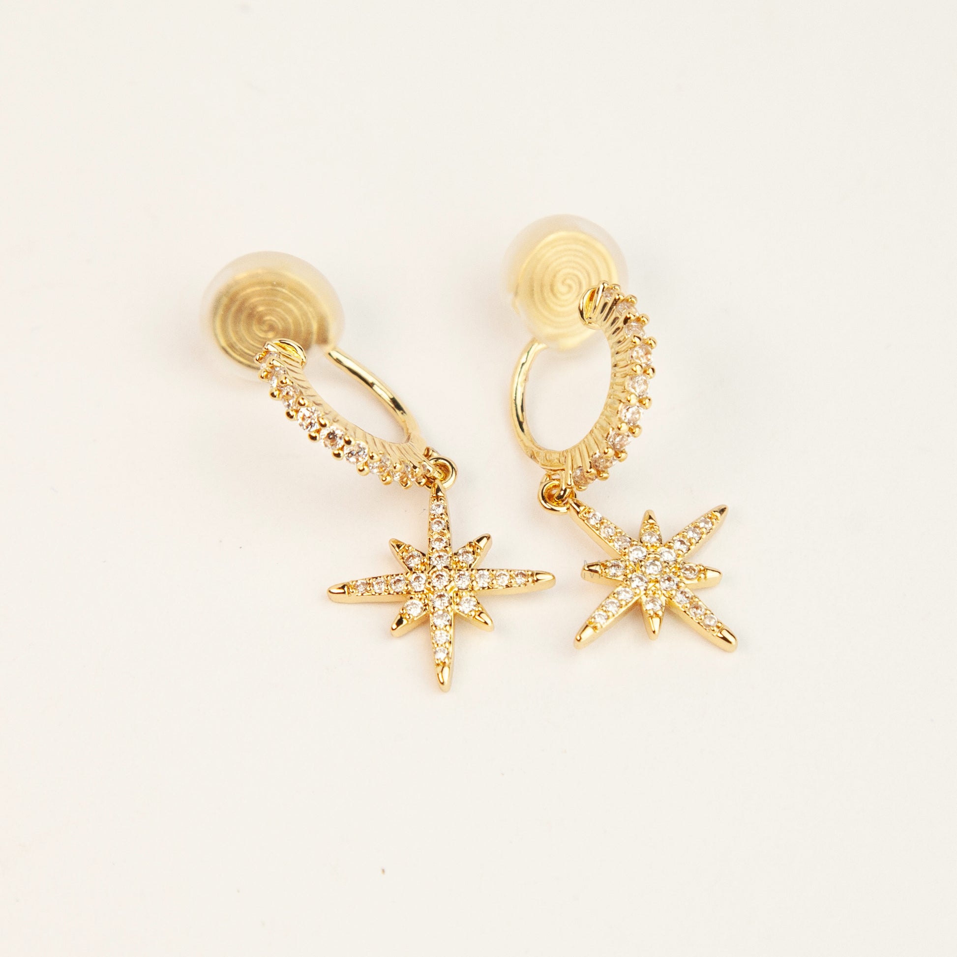 Gold and silver non-pierced clip-on dangle earrings with coil backs, featuring cubic zirconia paved hoops and celestial starburst drops.