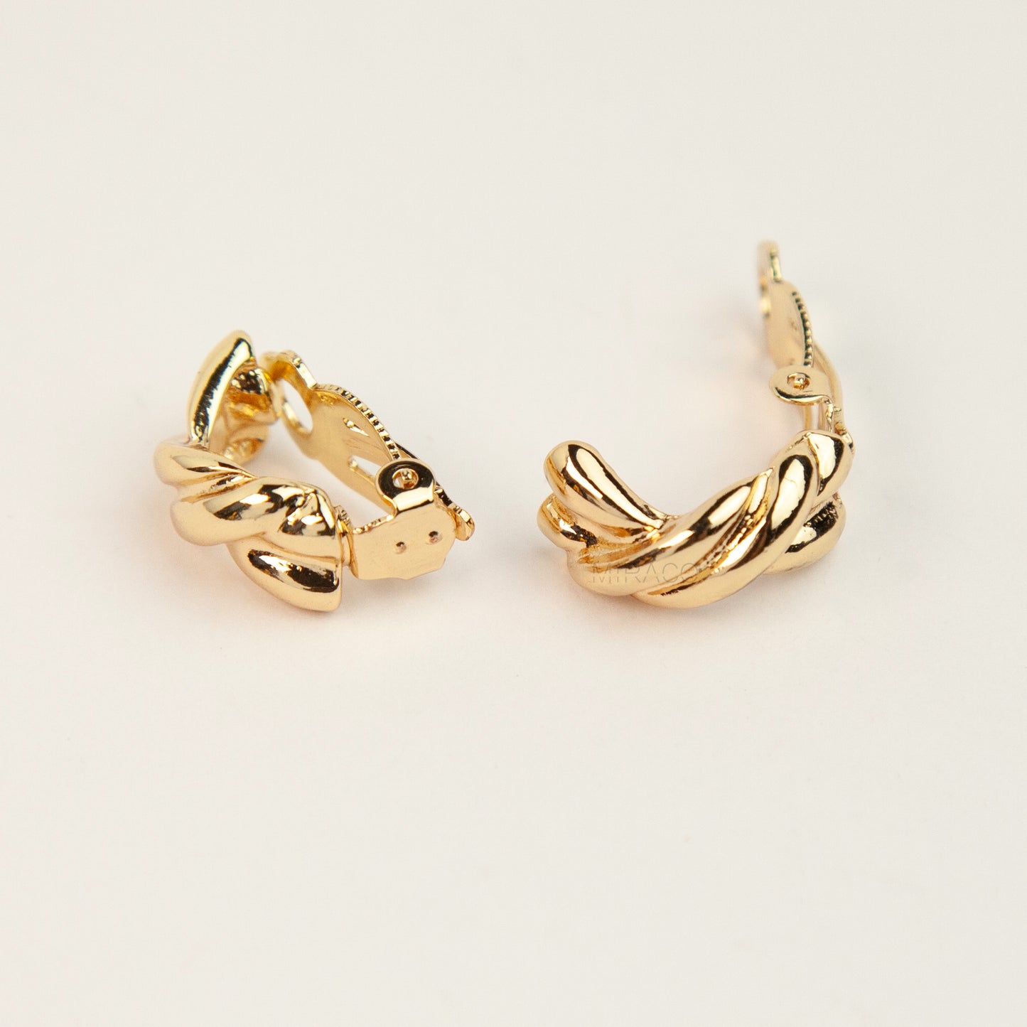 Chunky twisted crossover clip-on hoop earrings with paddle backs displayed in gold tones.
