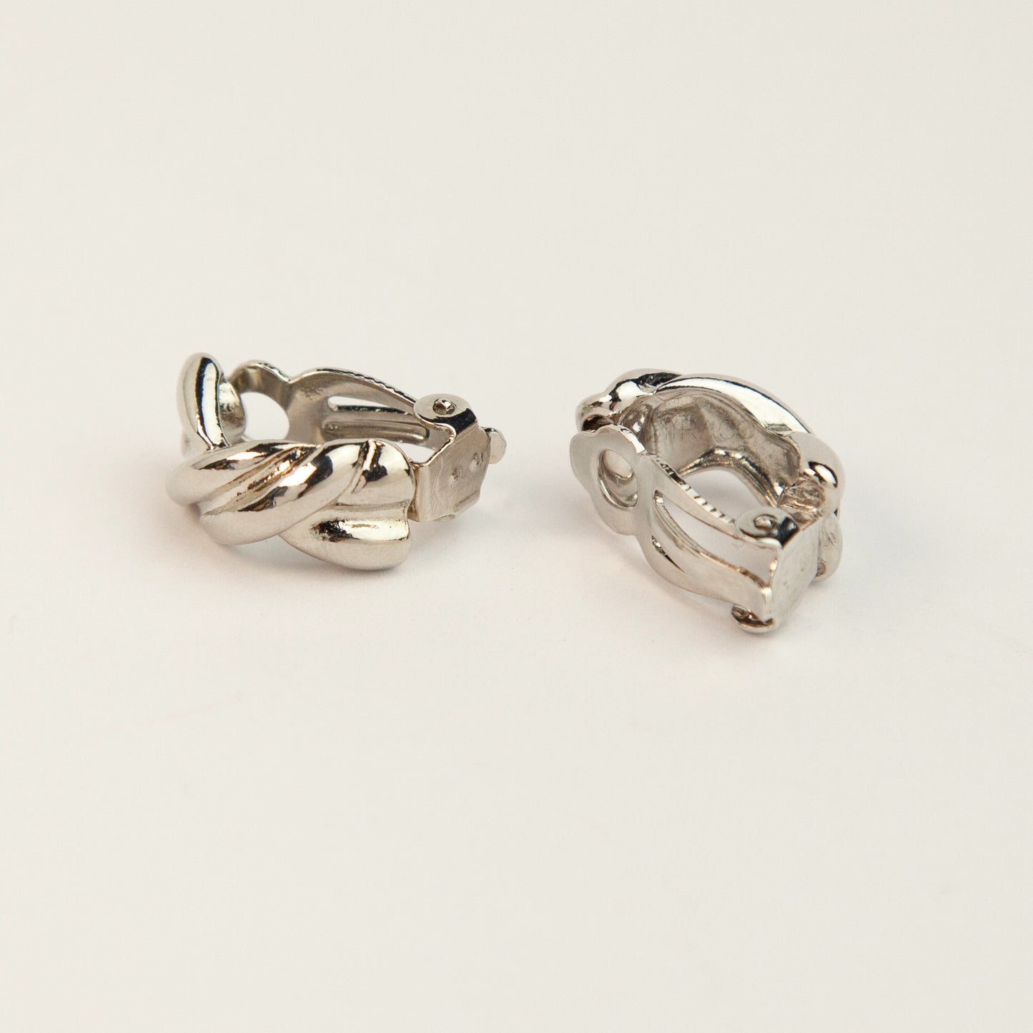 Chunky twisted crossover clip-on hoop earrings with paddle backs displayed in silver tones.