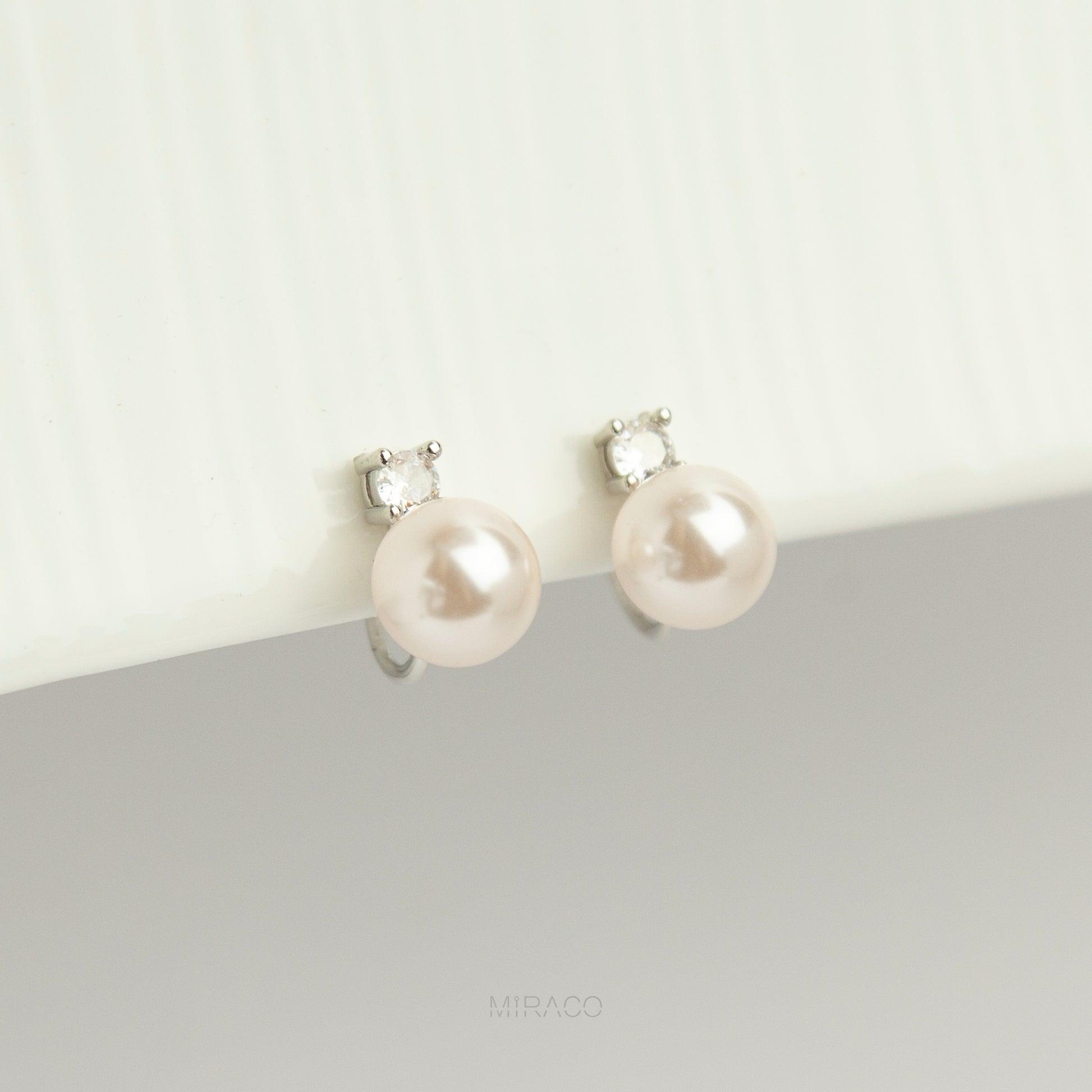 silver-tone non-pierced clip-on earring featuring a round white pearl drop suspended from a sparkling cubic zirconia solitaire with a coil back.
