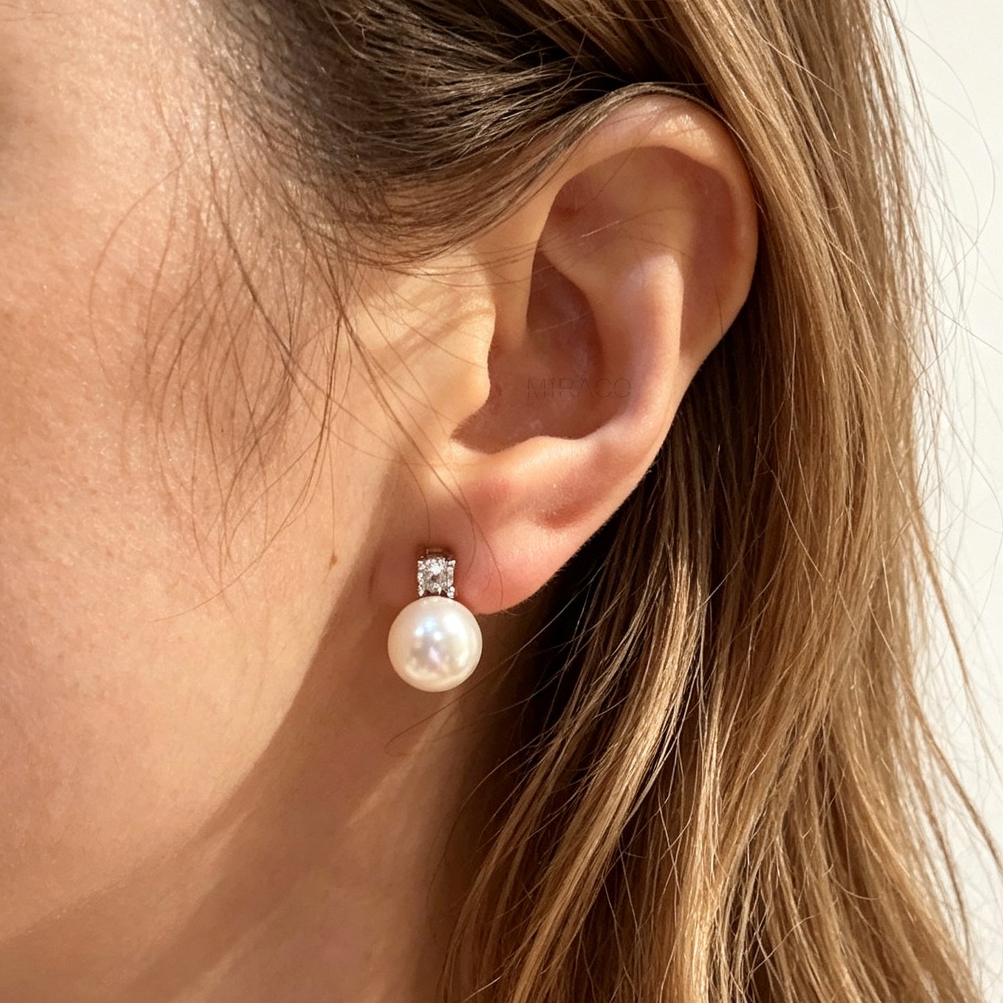 Woman wearing a silver-tone non-pierced clip-on earring featuring a round white pearl drop suspended from a sparkling cubic zirconia solitaire with a coil back.