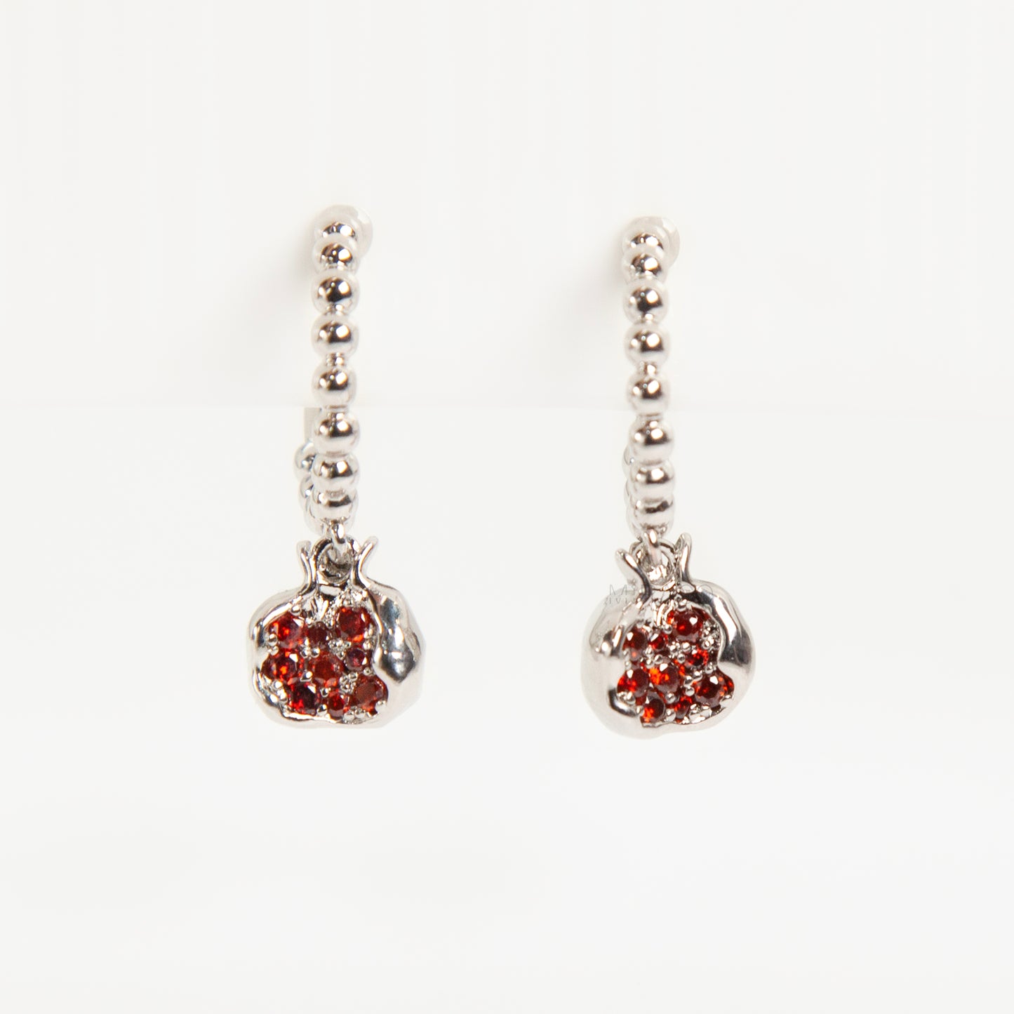 Pair of silver-tone hoop clip-on earrings with a beaded design and a red CZ-encrusted pomegranate charm dangle. Shows the Coil Back mechanism.