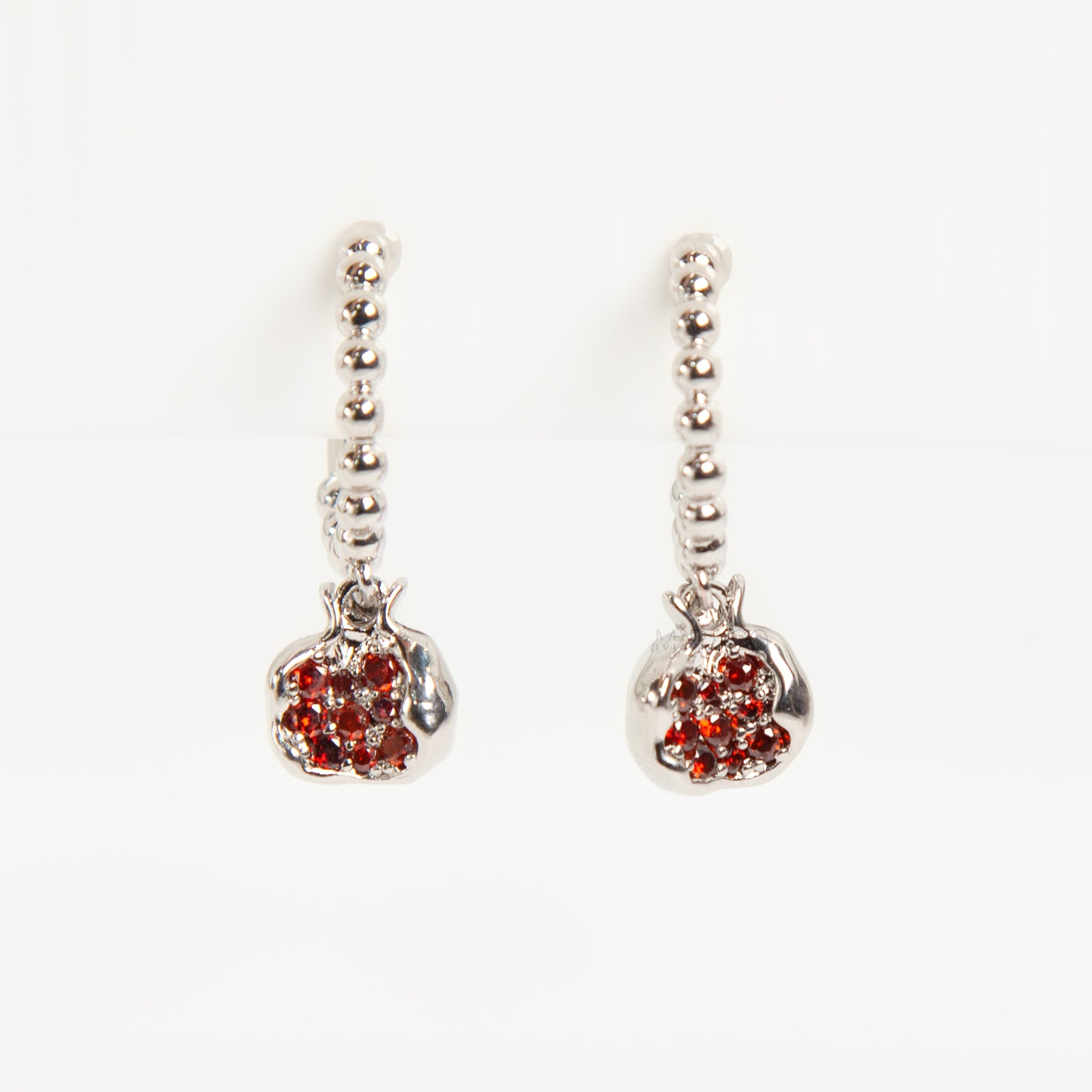 Pair of silver-tone hoop clip-on earrings with a beaded design and a red CZ-encrusted pomegranate charm dangle. Shows the Coil Back mechanism.