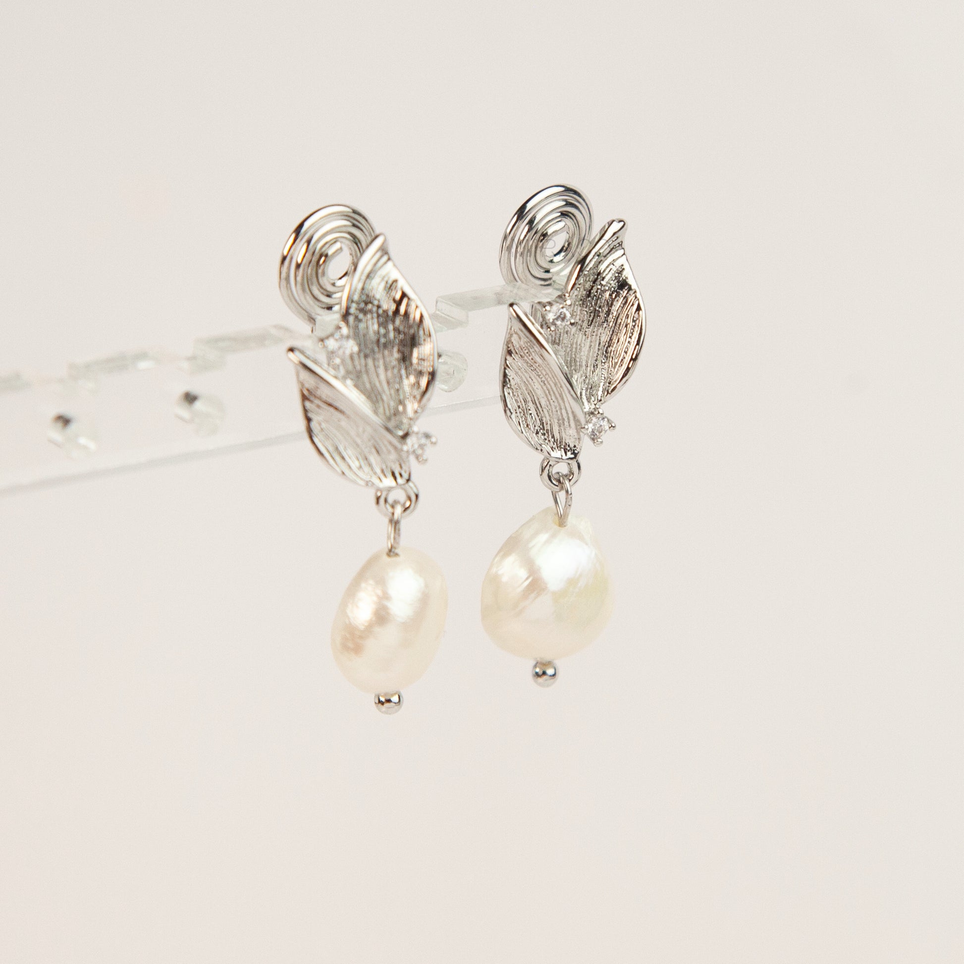 Pair of silver-tone leaf motif clip-on earrings with natural white baroque pearl drops and spiral coil backs displayed on a white background.
