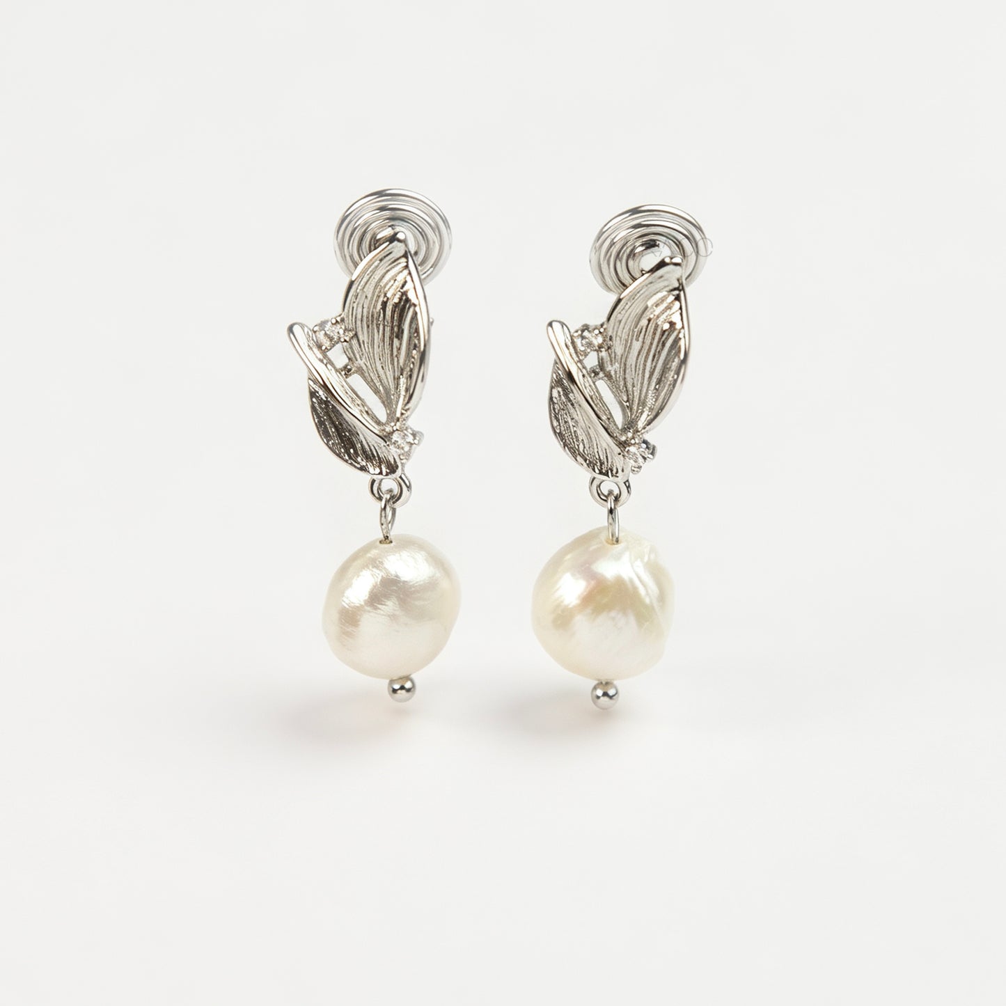 Pair of silver-tone leaf motif clip-on earrings with natural white baroque pearl drops and spiral coil backs displayed on a white background.
