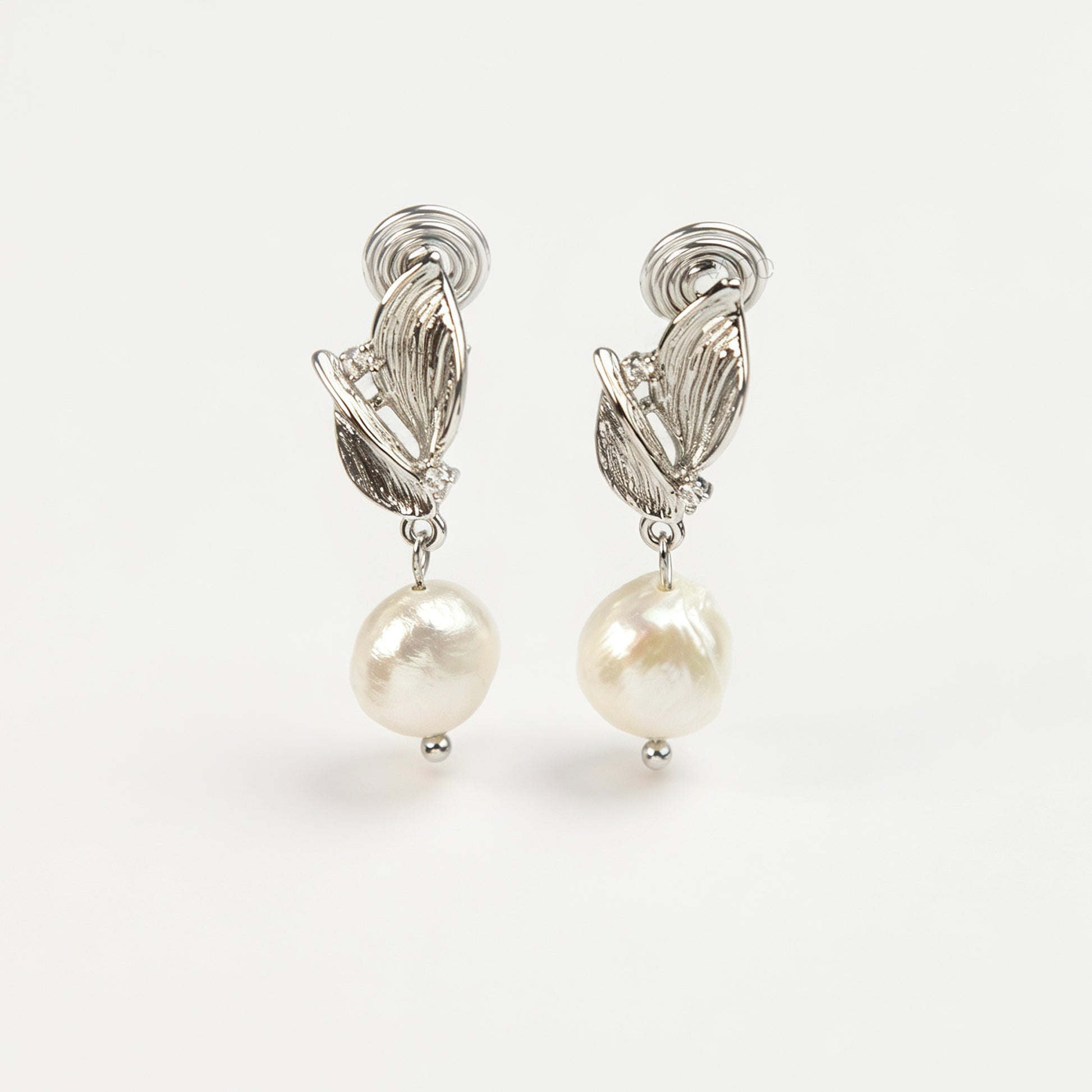 Pair of silver-tone leaf motif clip-on earrings with natural white baroque pearl drops and spiral coil backs displayed on a white background.
