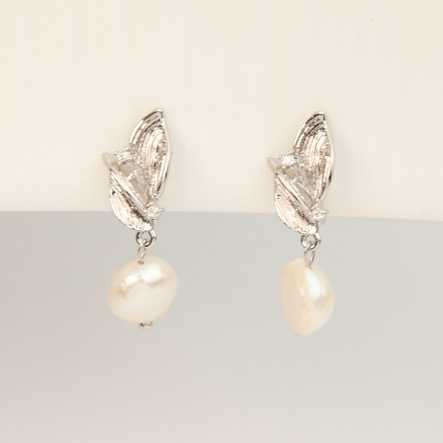 Pair of silver-tone leaf motif clip-on earrings with natural white baroque pearl drops and spiral coil backs displayed on a white background.