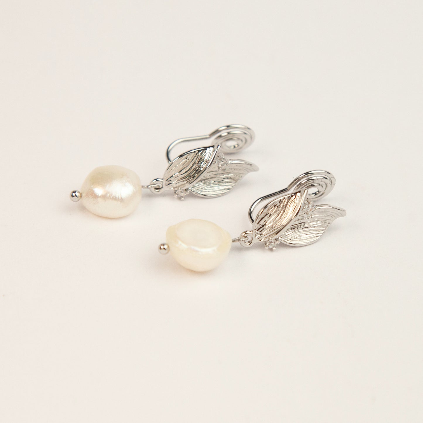 Pair of silver-tone leaf motif clip-on earrings with natural white baroque pearl drops and spiral coil backs displayed on a white background.