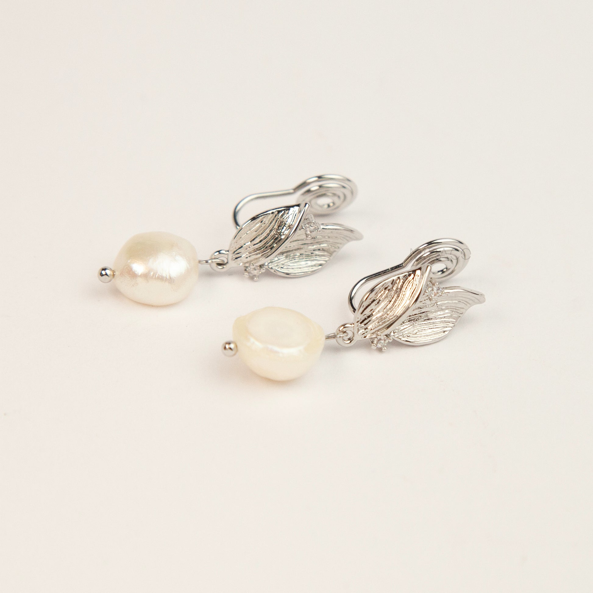 Pair of silver-tone leaf motif clip-on earrings with natural white baroque pearl drops and spiral coil backs displayed on a white background.