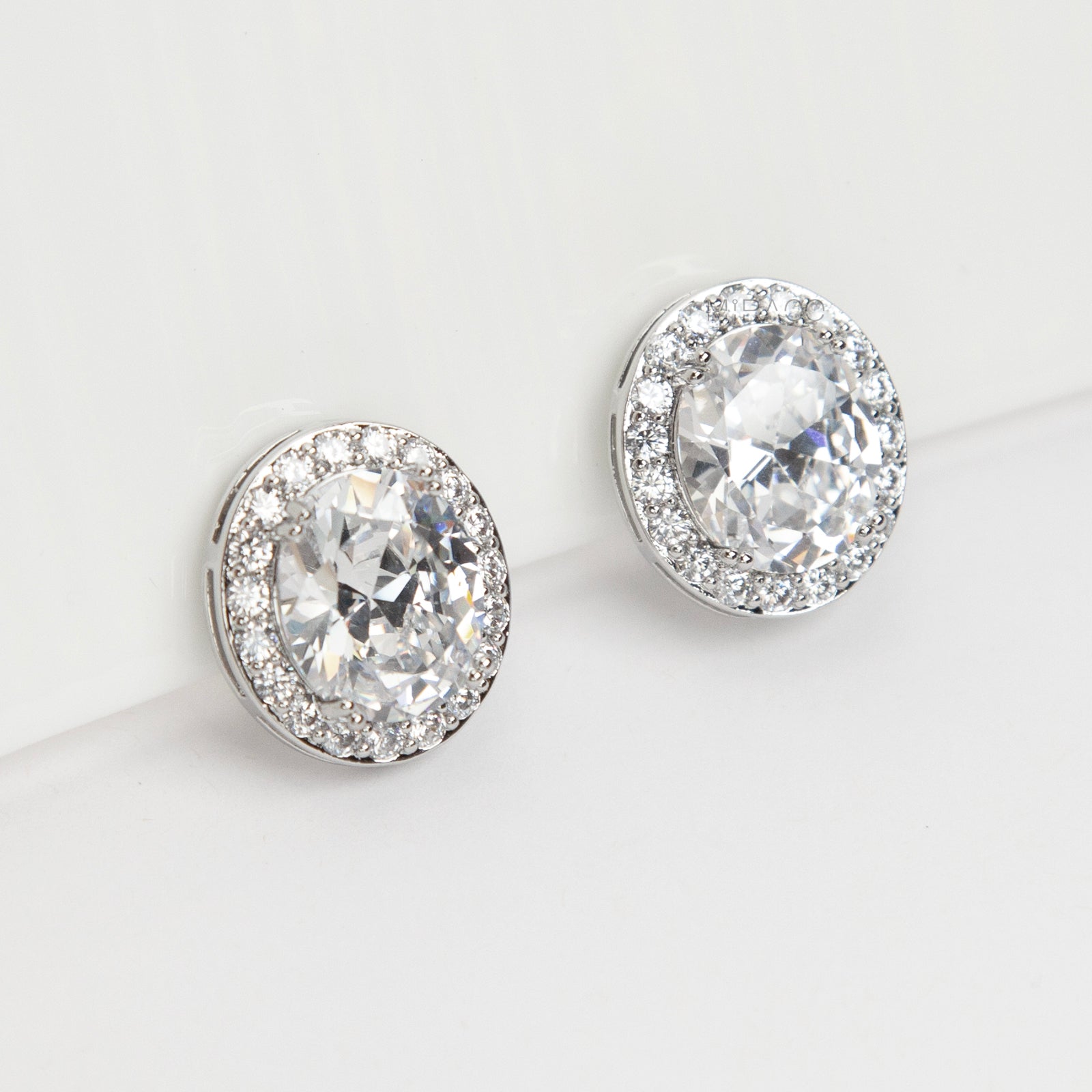 Pair of silver-tone oval halo clip-on stud earrings featuring a large central brilliant-cut cubic zirconia stone surrounded by a circle of small pave-set crystals.