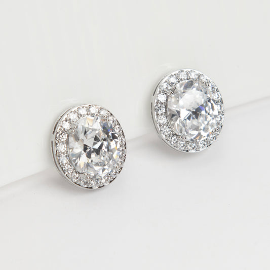 Pair of silver-tone oval halo clip-on stud earrings featuring a large central brilliant-cut cubic zirconia stone surrounded by a circle of small pave-set crystals.