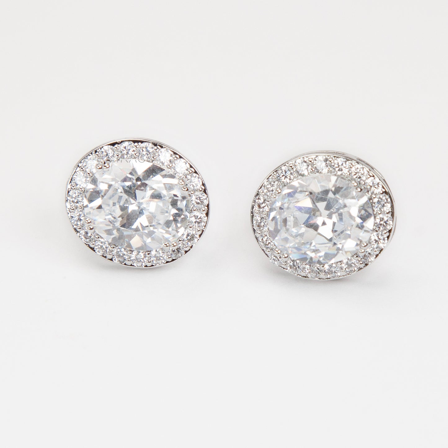 Pair of silver-tone oval halo clip-on stud earrings featuring a large central brilliant-cut cubic zirconia stone surrounded by a circle of small pave-set crystals.