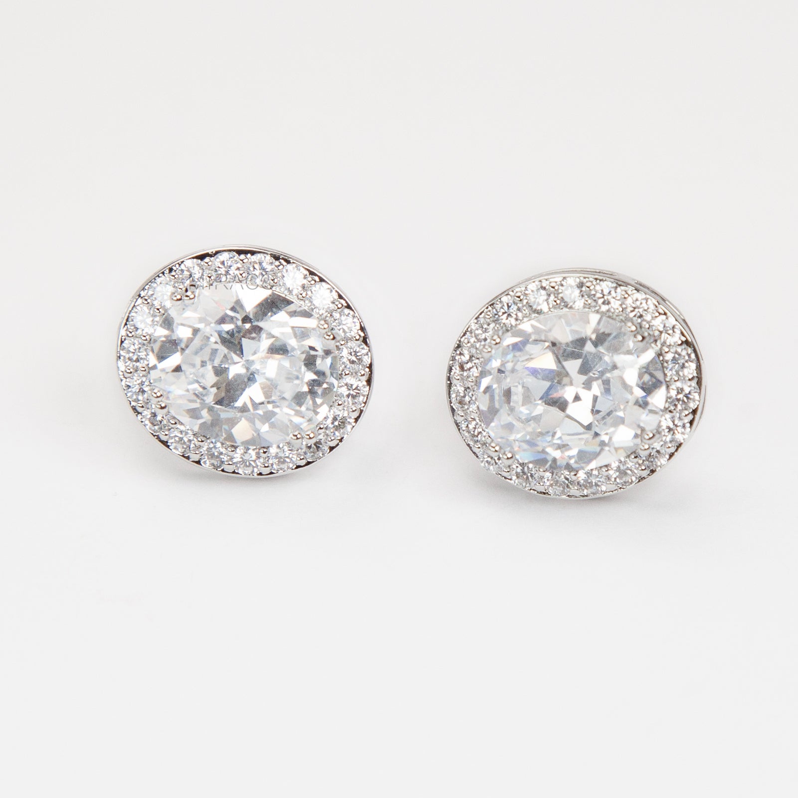 Pair of silver-tone oval halo clip-on stud earrings featuring a large central brilliant-cut cubic zirconia stone surrounded by a circle of small pave-set crystals.