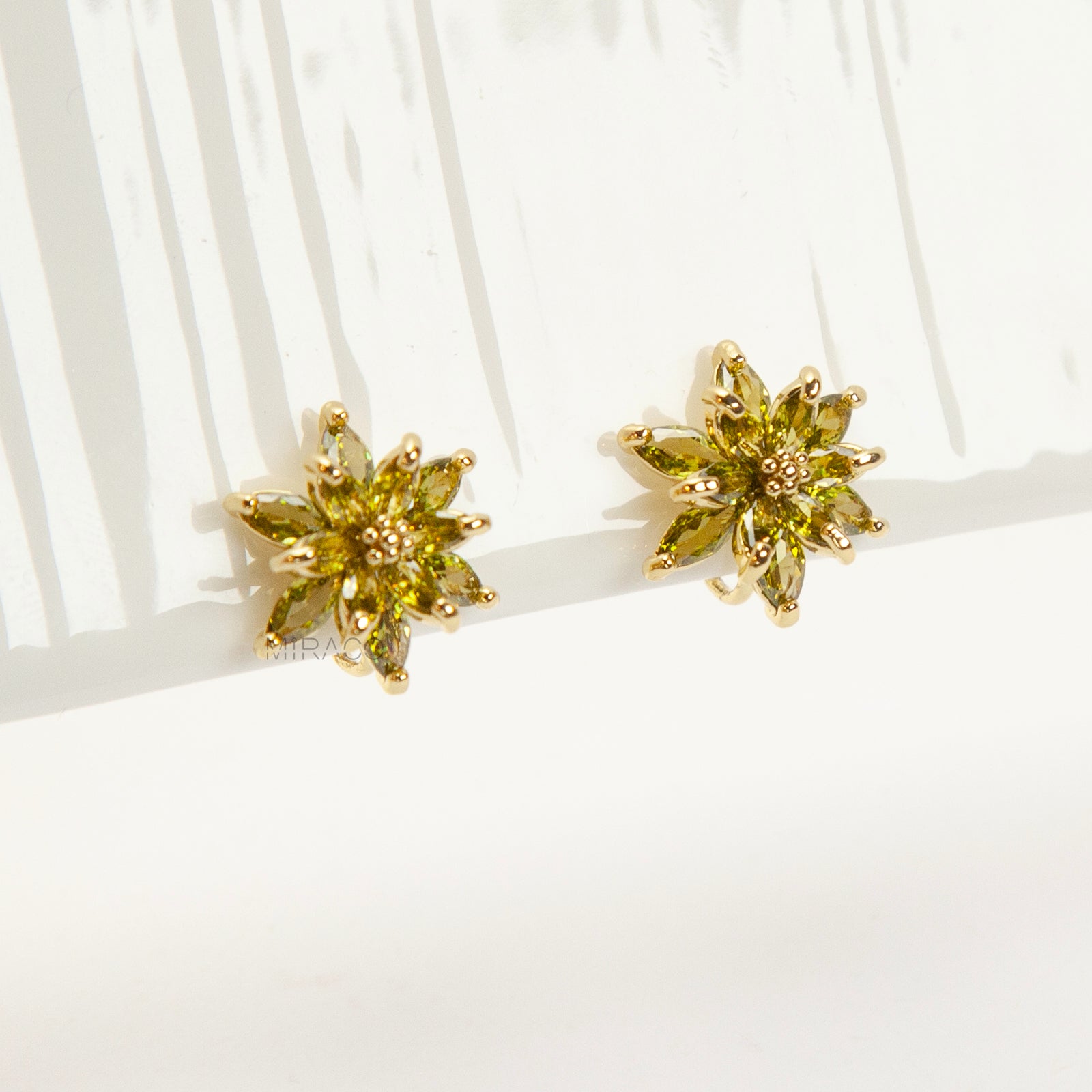 Pair of gold-tone clip-on earrings shaped like a flower or starburst, featuring marquise-cut peridot green crystals radiating from the center.