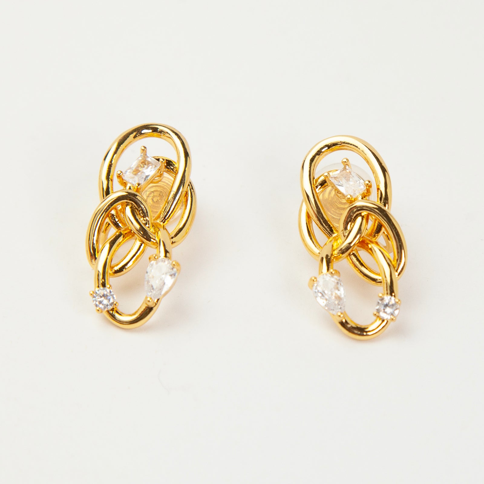 Close-up of a pair of gold interlocking double-knot clip-on earrings featuring two brilliant cut cubic zirconia stones, displayed on a white surface.