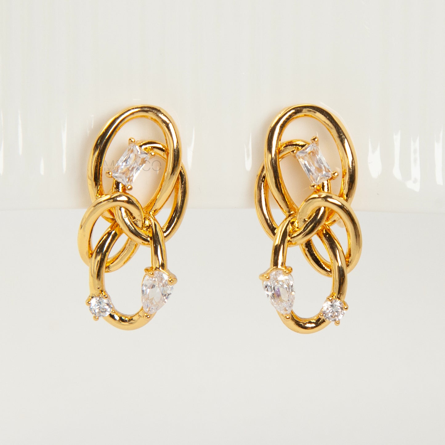 Close-up of a pair of gold interlocking double-knot clip-on earrings featuring two brilliant cut cubic zirconia stones, displayed on a white surface.