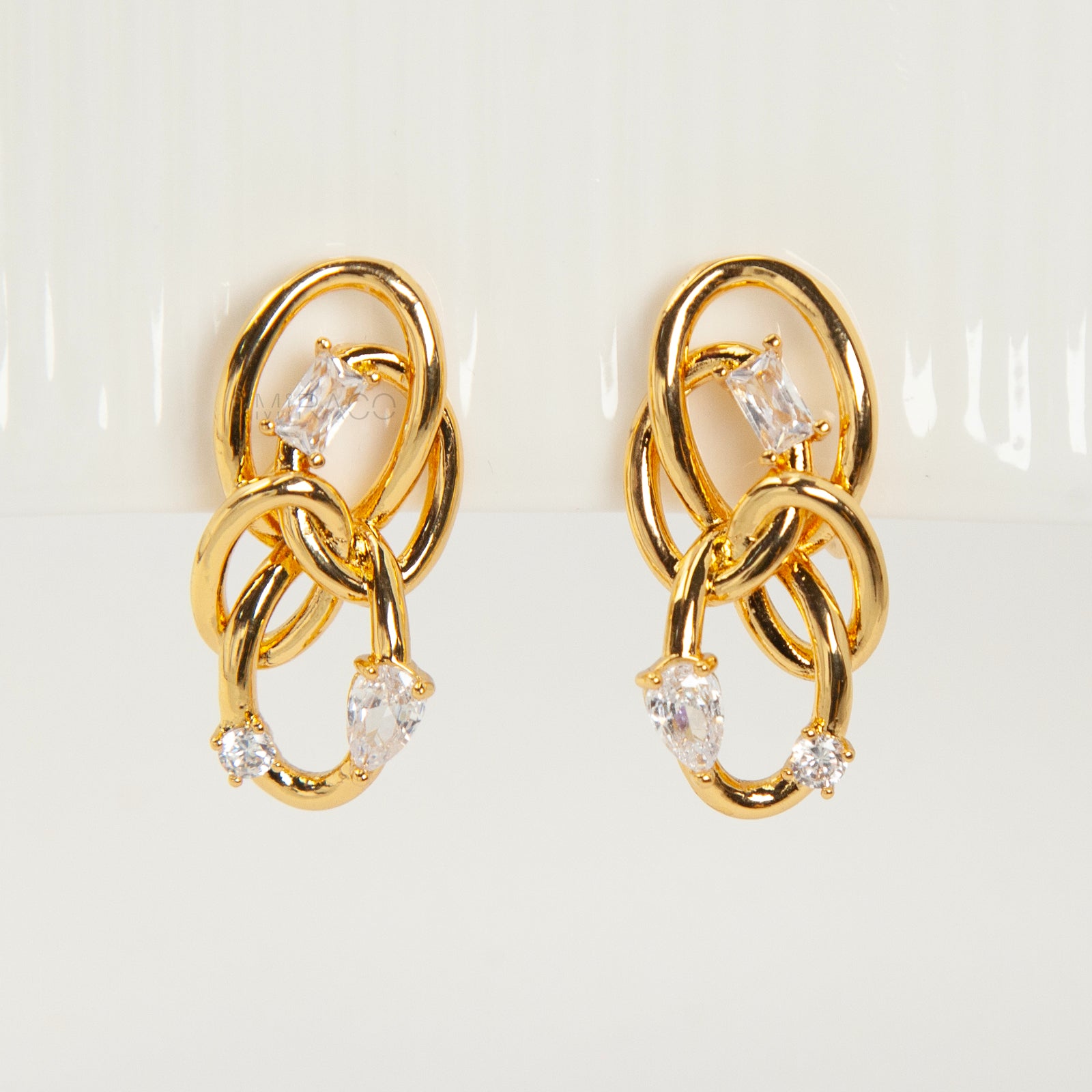 Close-up of a pair of gold interlocking double-knot clip-on earrings featuring two brilliant cut cubic zirconia stones, displayed on a white surface.